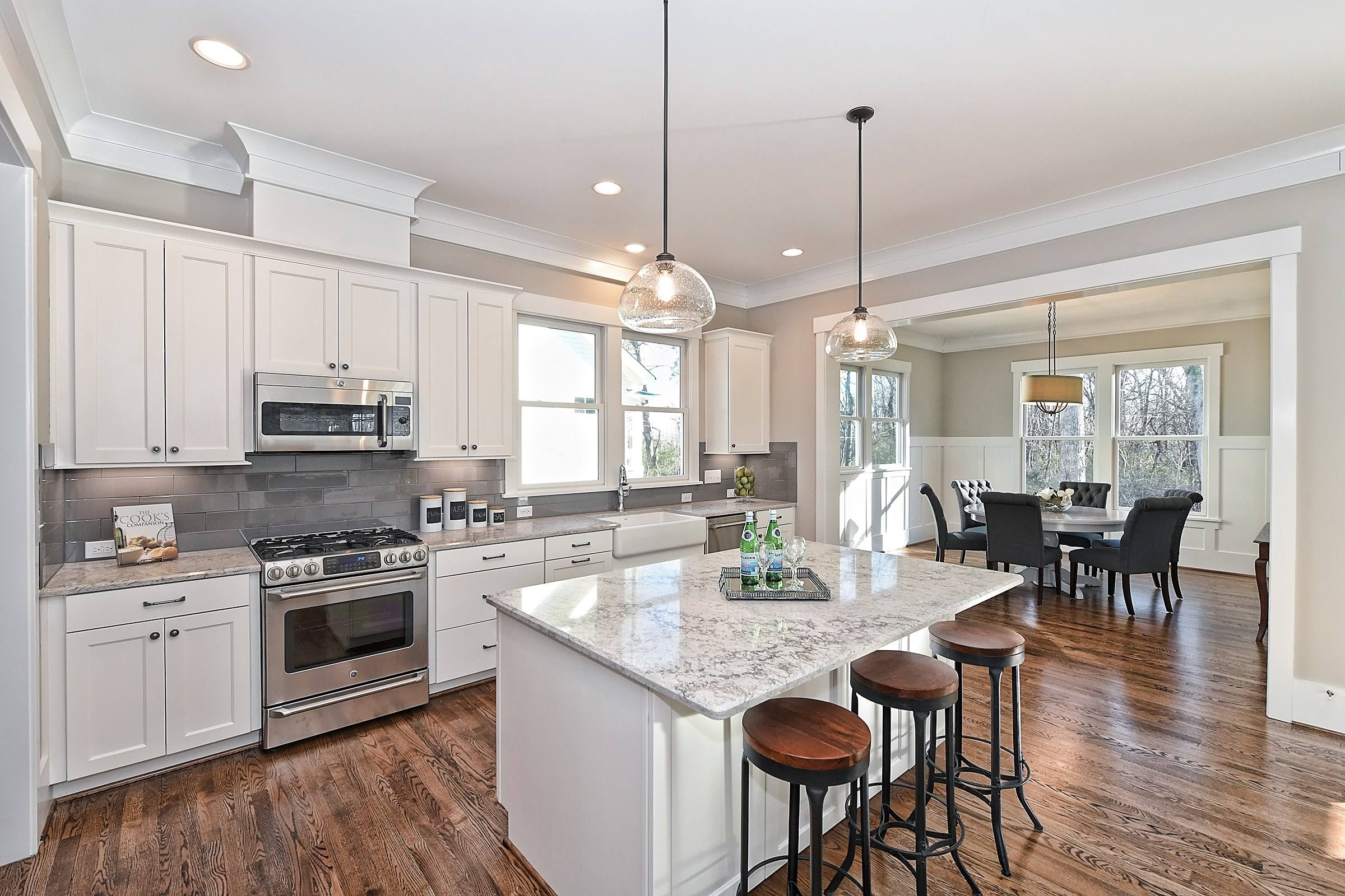 White kitchen with an island, granite counters, stainless appliances, and bar stools, open to a dining area