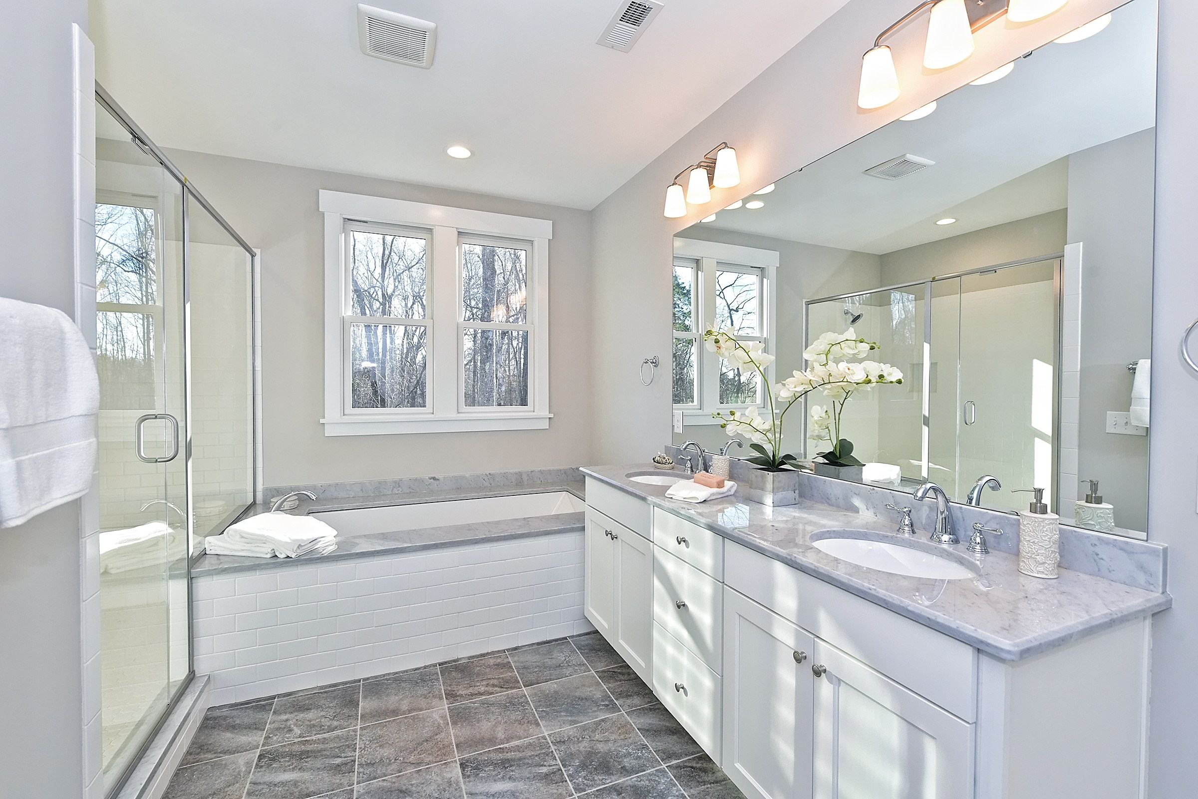 Primary bathroom with a soaking tub under a window, a glass shower, and a long white double vanity