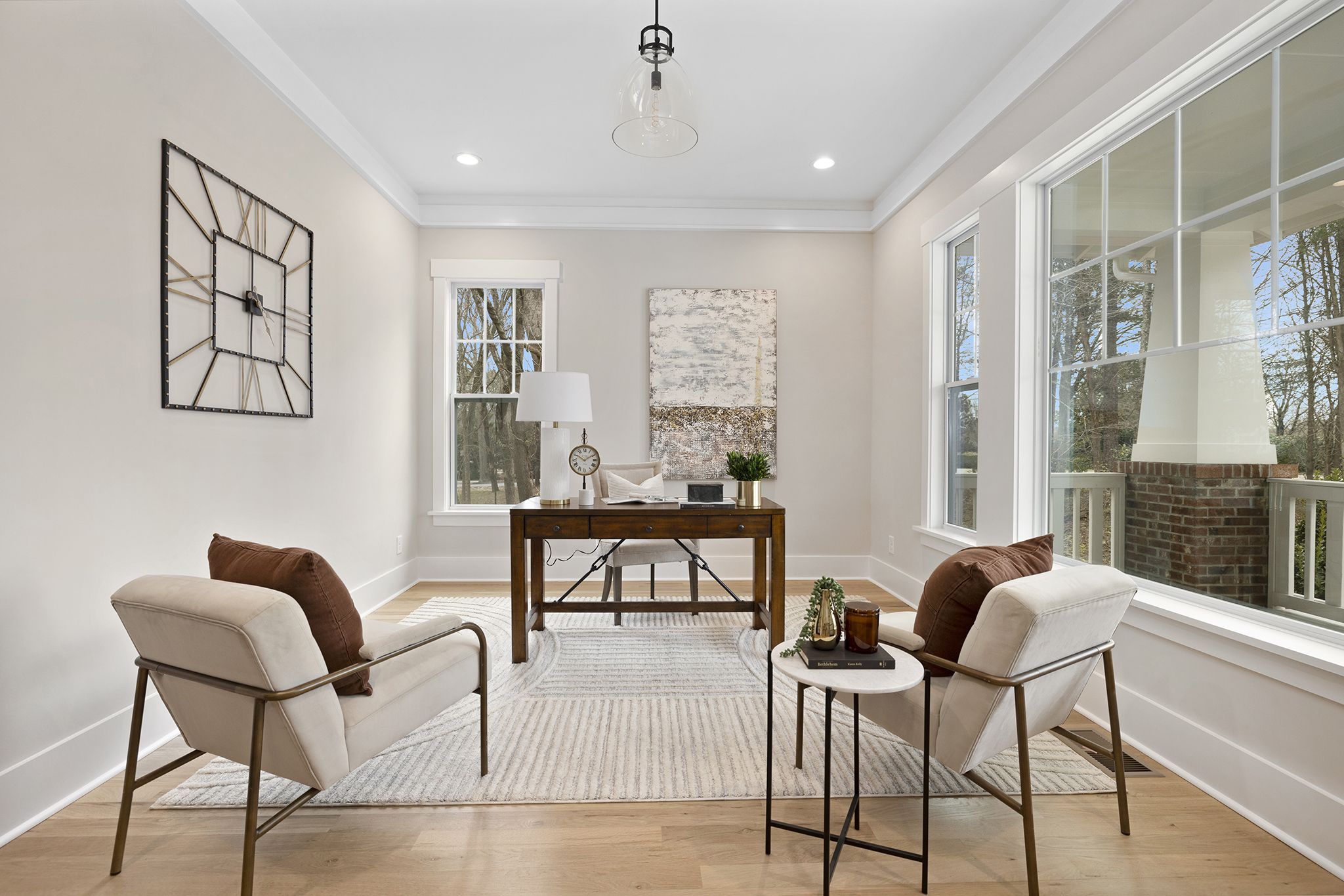 Home office with a desk, two lounge chairs, a pendant light, and tall windows