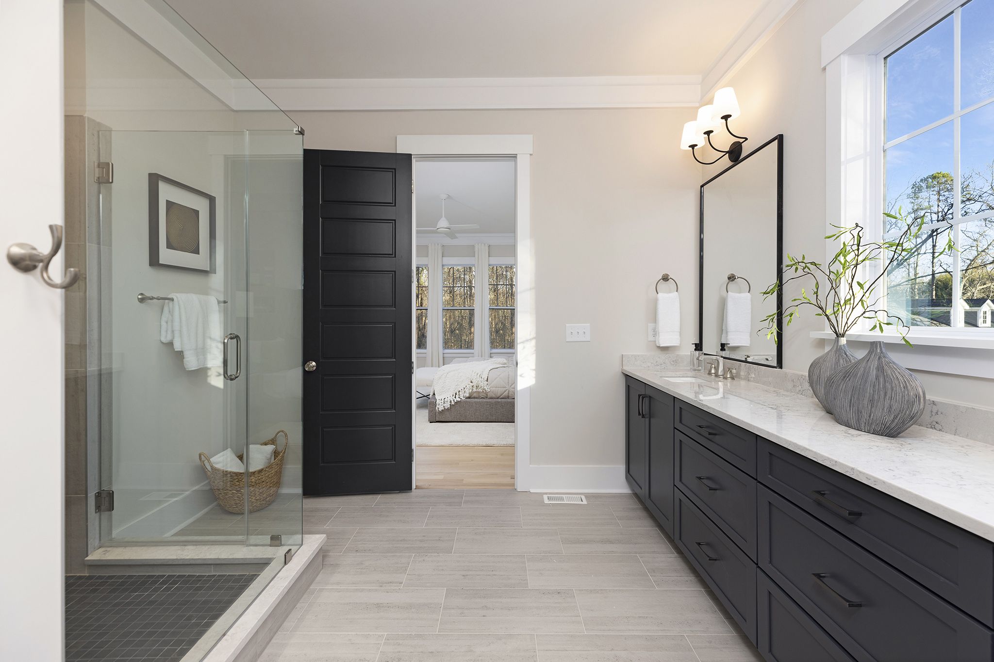 Primary bathroom with a glass shower, a long vanity with dark cabinets, and a view into the bedroom