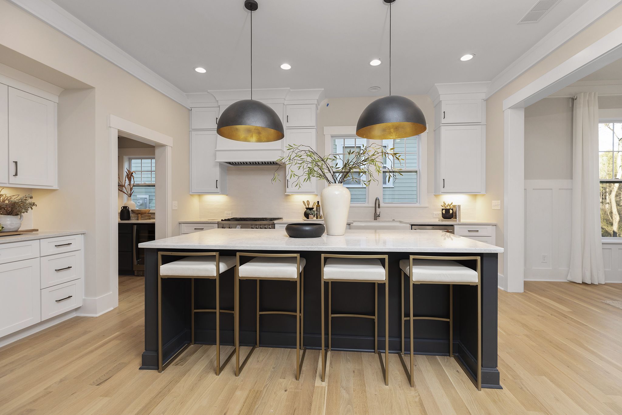 White kitchen with a dark island, four counter stools, and two black-and-gold dome pendants