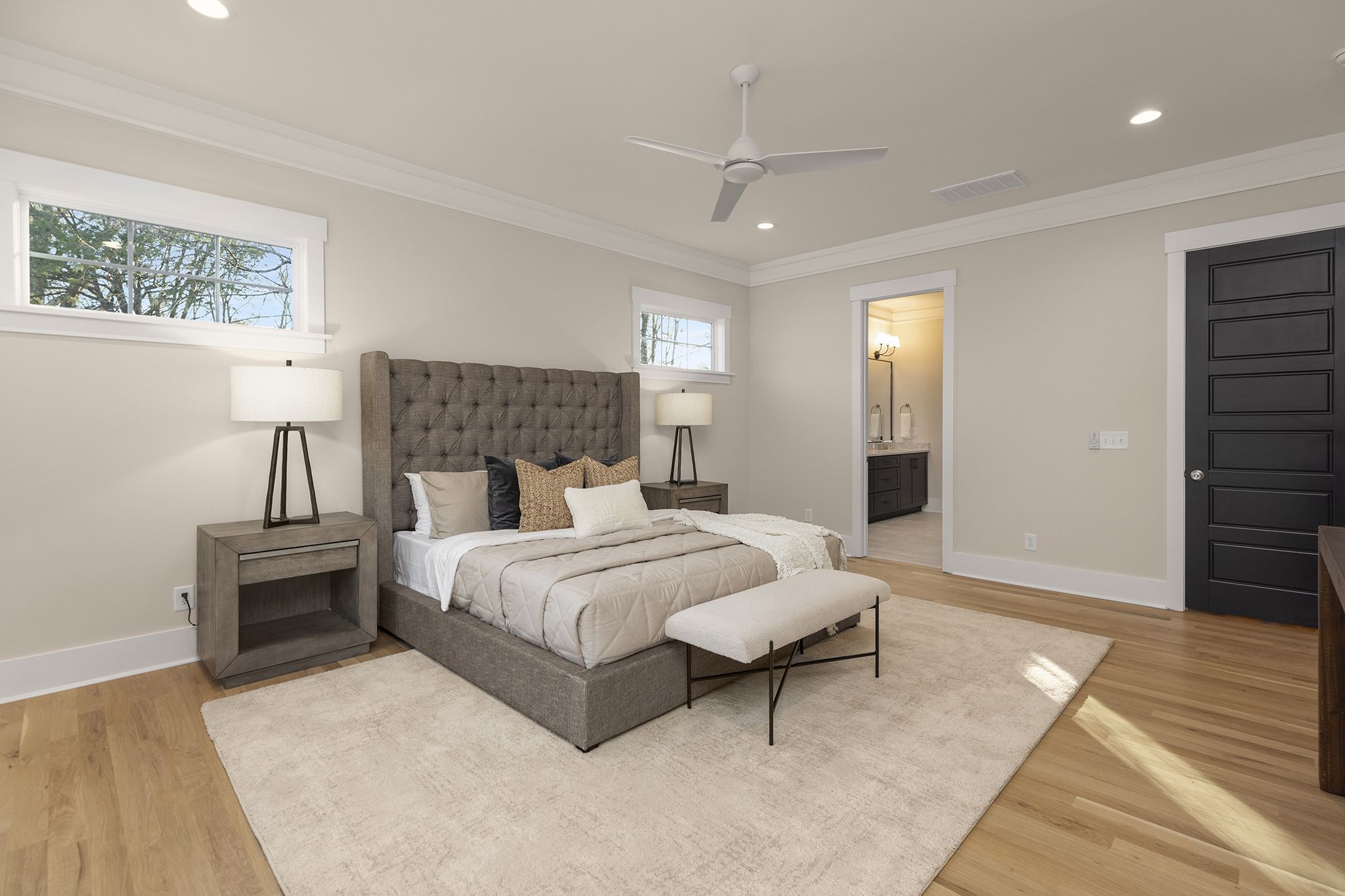 Primary bedroom with an upholstered bed, a ceiling fan, transom windows, and a doorway to the bathroom