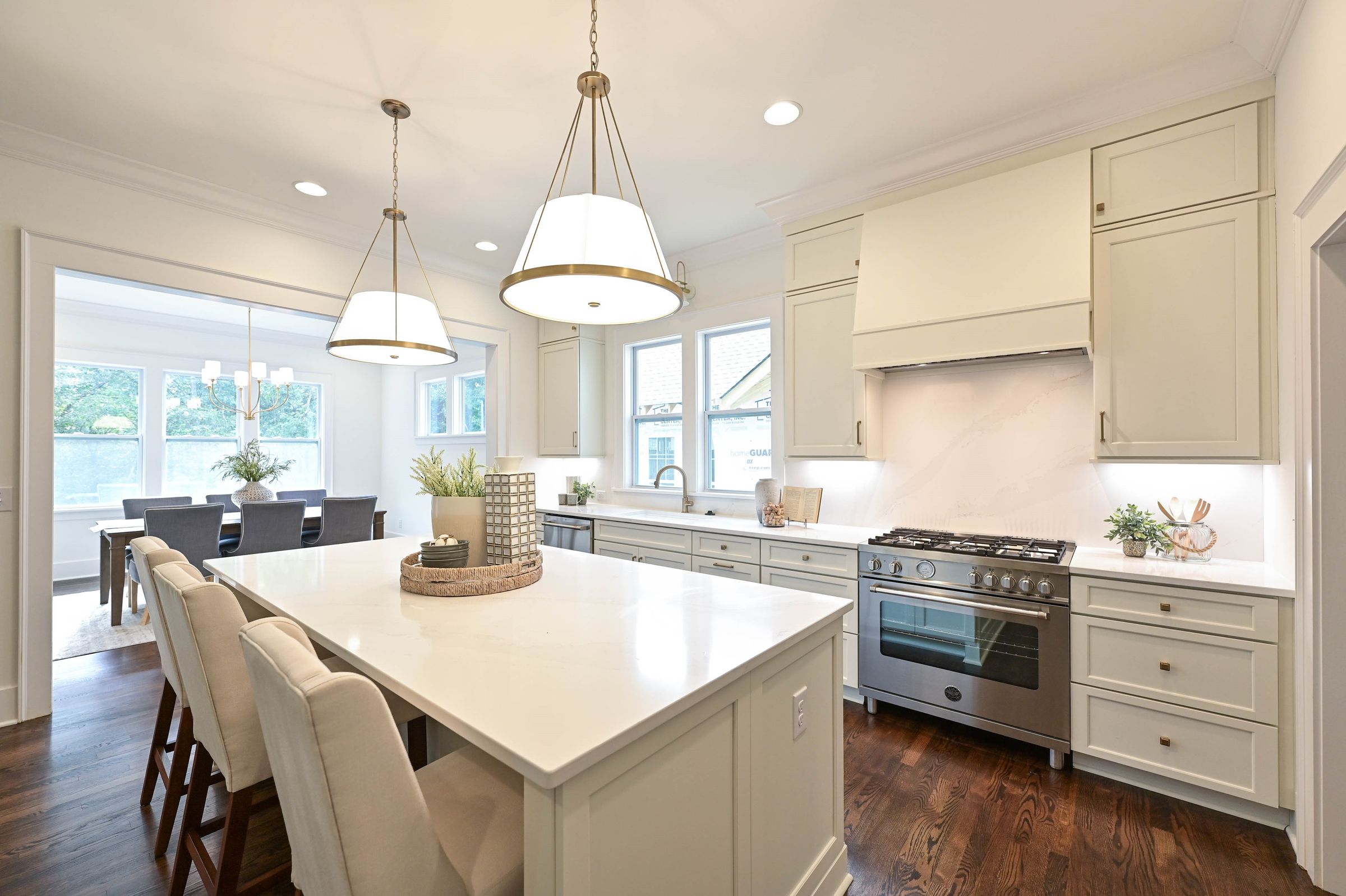 Cream kitchen with a large island, gas range, brass pendant lights, and a dining area with big windows