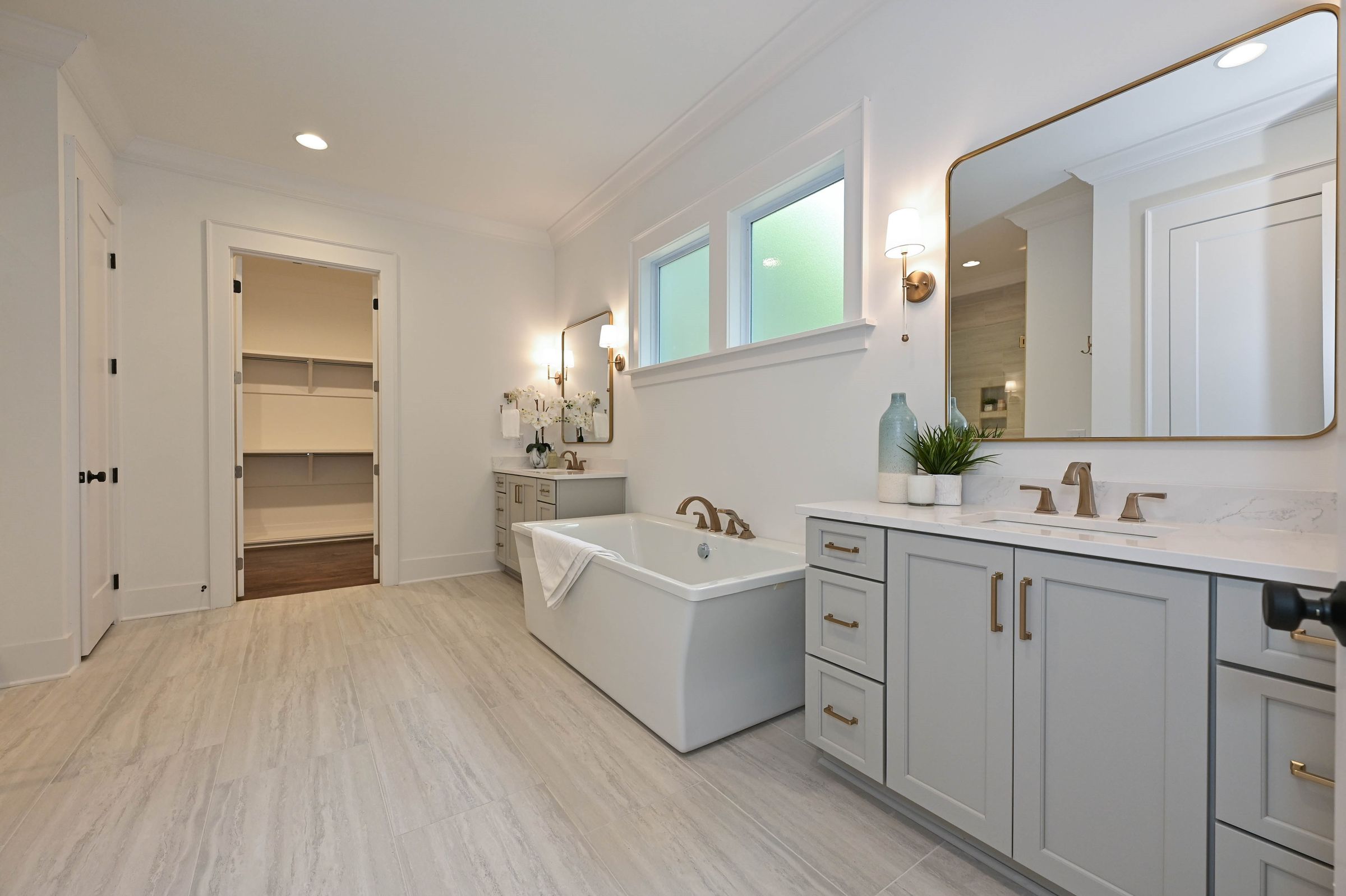 Primary bathroom with a freestanding tub, a gray double vanity, and a walk-in closet