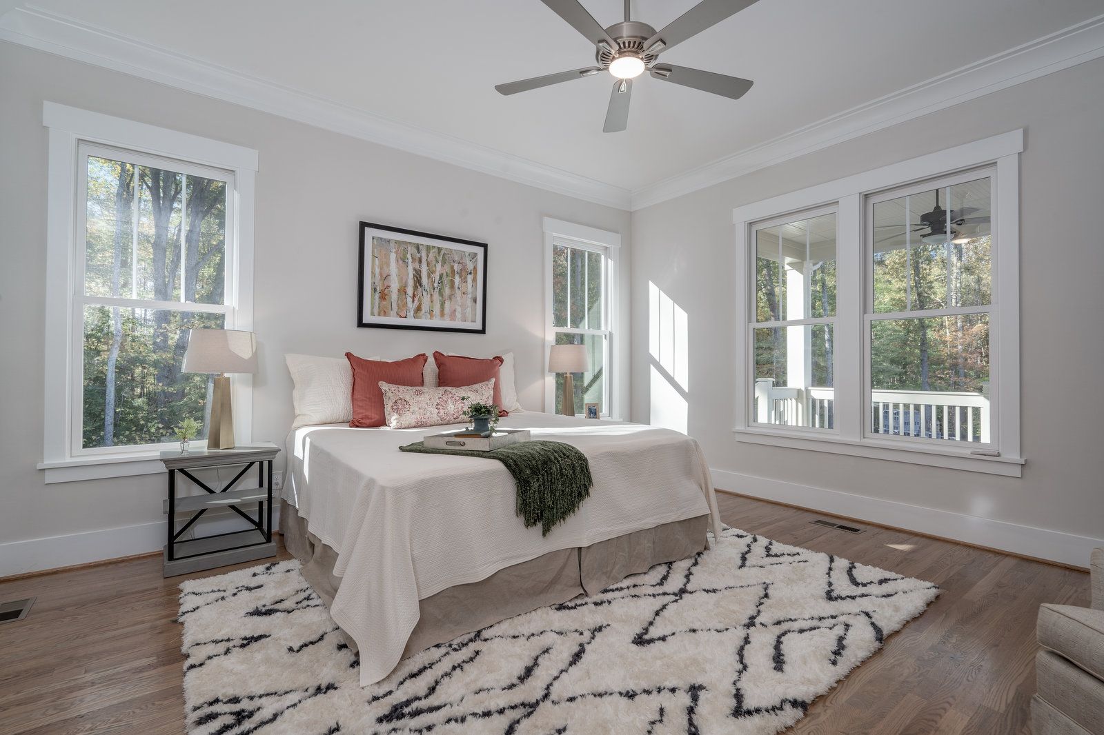 Primary bedroom with a ceiling fan, hardwood floors, a patterned rug, and windows onto a porch
