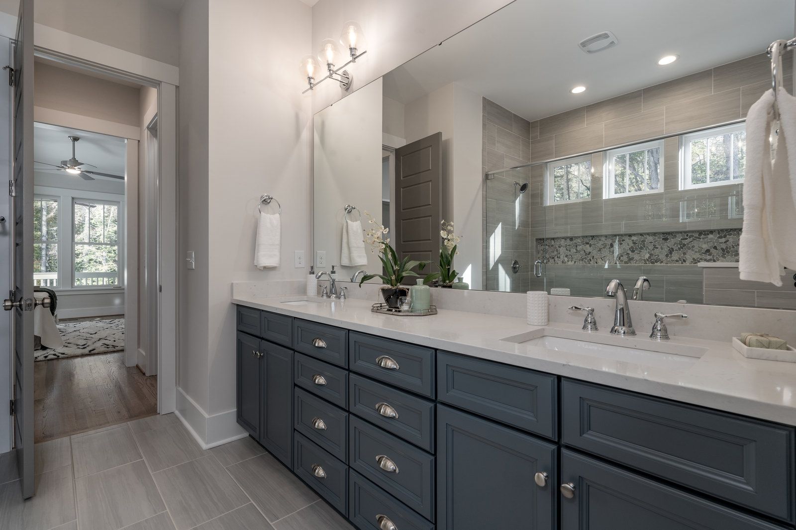 Bathroom with a long navy double vanity, a large mirror, and a tiled shower
