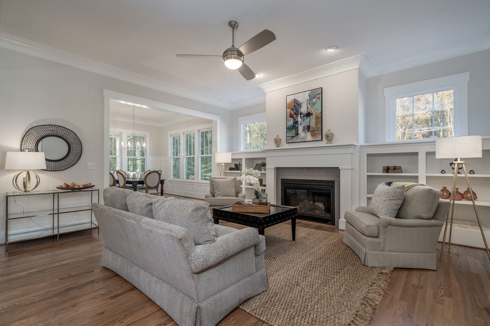 Living room with a fireplace and built-ins, a ceiling fan, and an opening to a sunny dining room