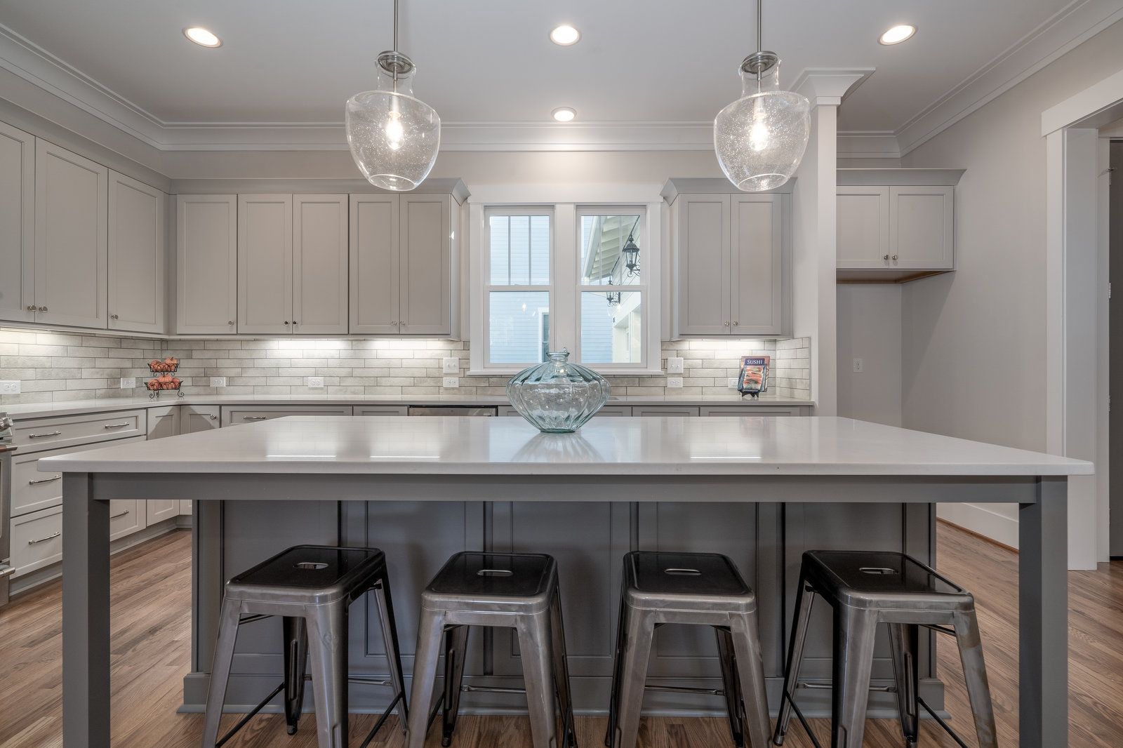 Kitchen with a large gray island, metal counter stools, glass pendants, and white cabinets