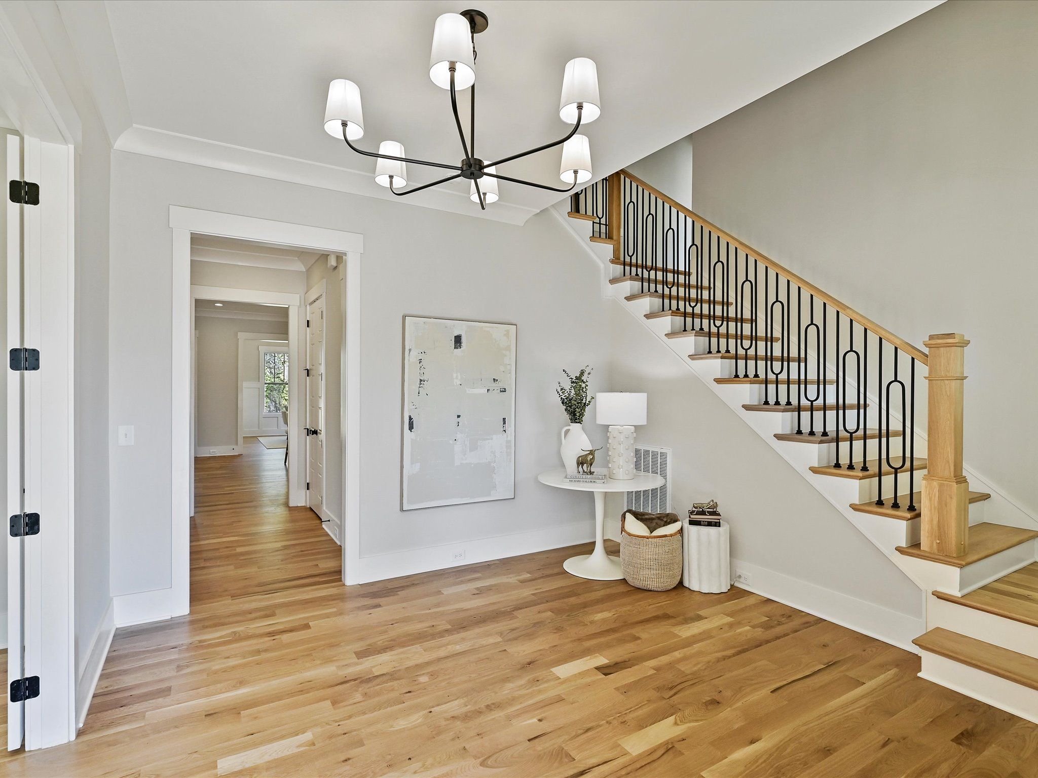 Entry hall with a modern chandelier, an open staircase with black metal balusters, and light wood floors