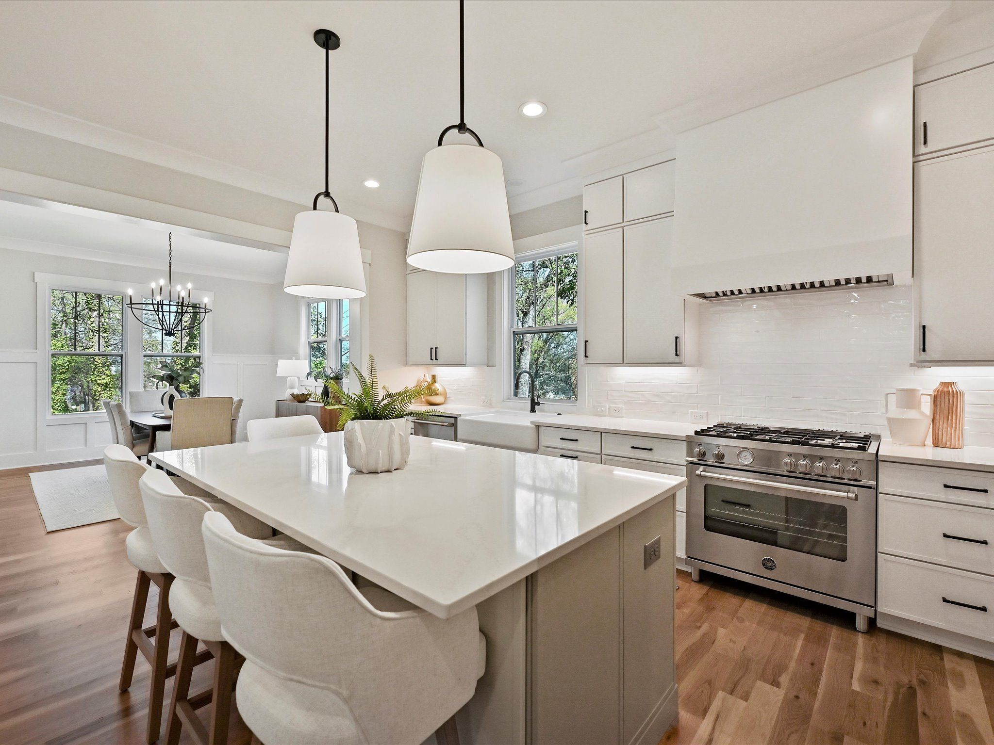 White kitchen with an island, pendant lights, a range hood, and a dining area beyond