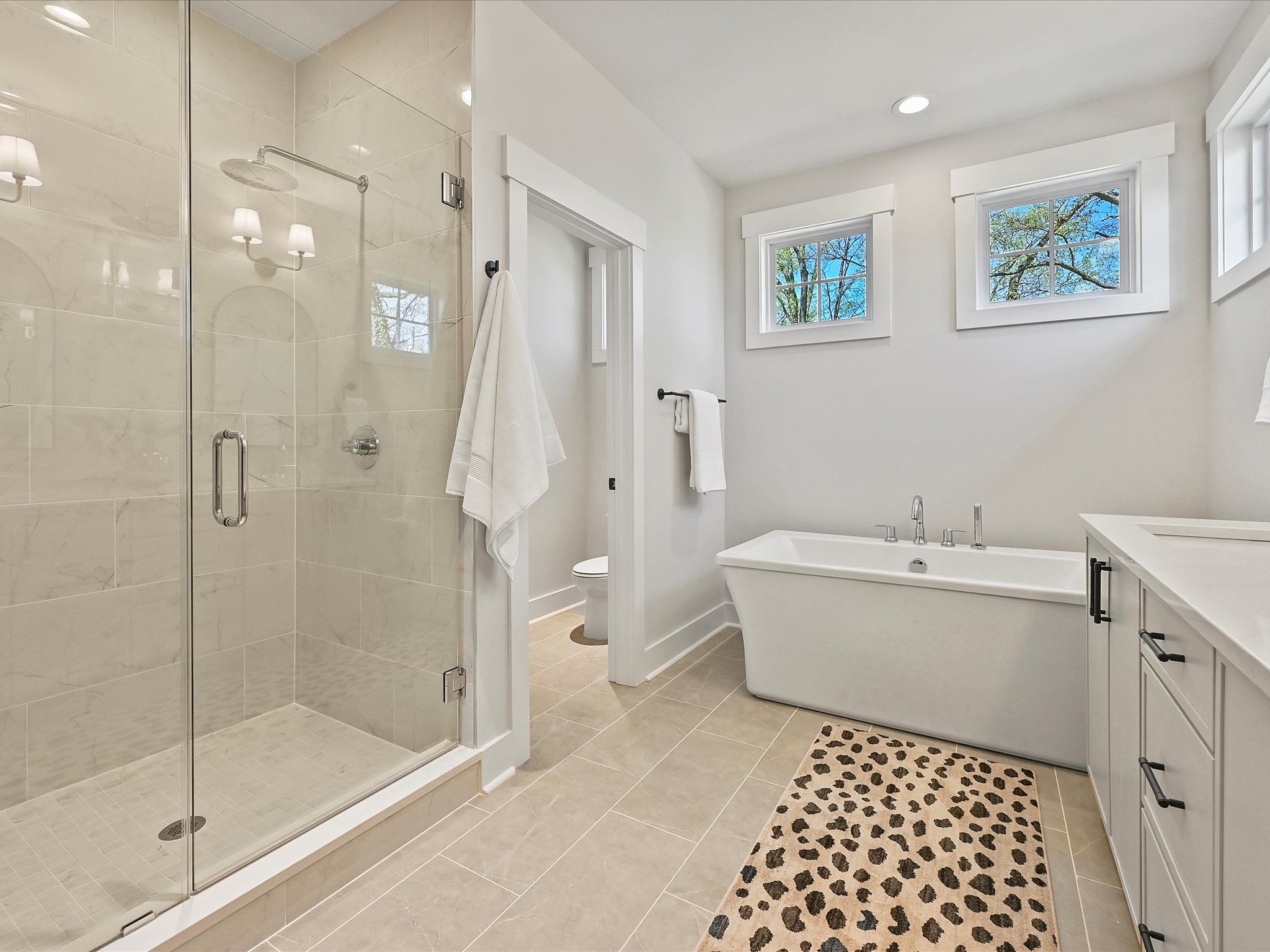 Primary bathroom with a frameless glass shower, a freestanding tub, and high windows