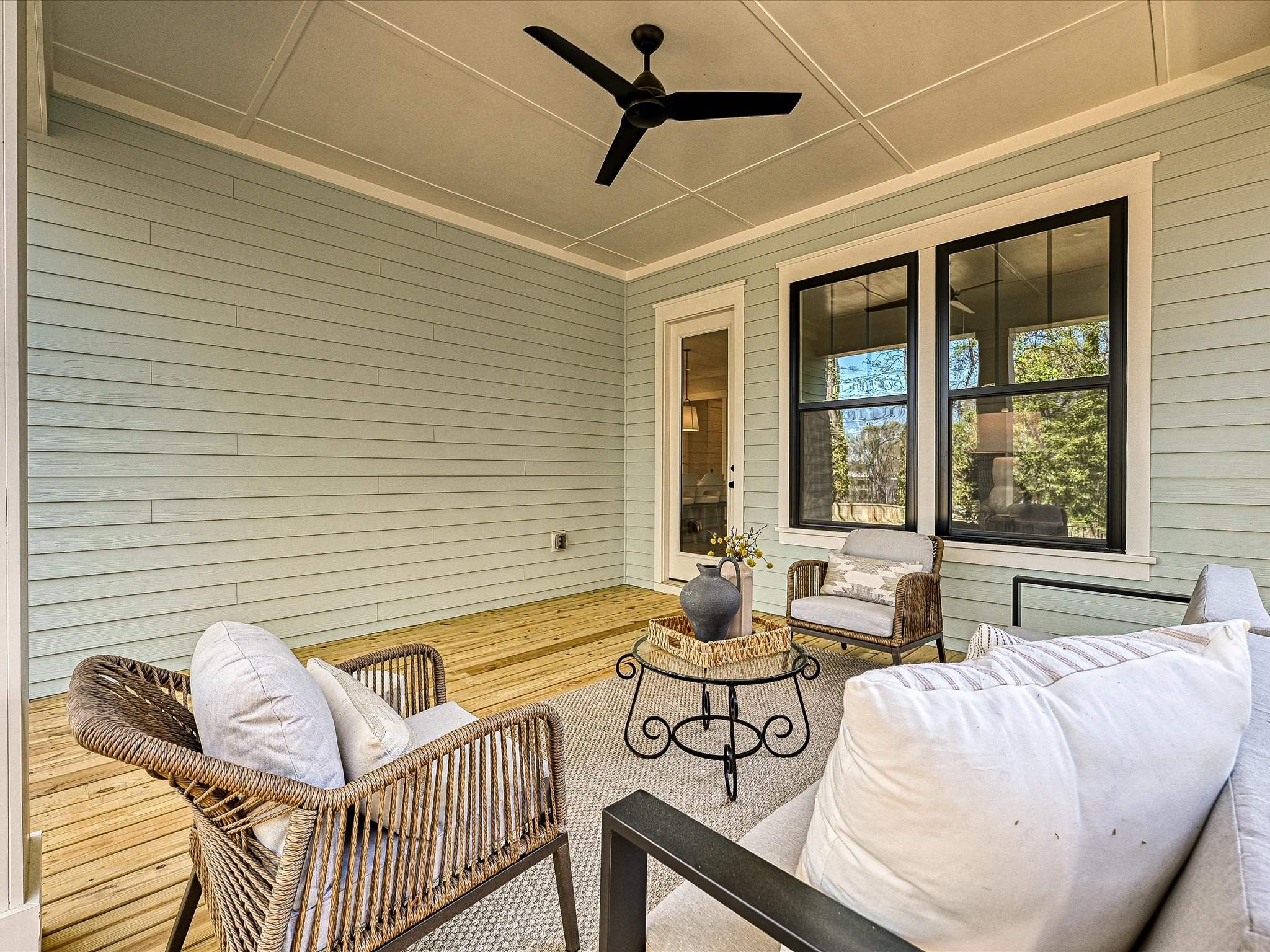 Screened back porch with a wood floor, ceiling fan, and wicker seating