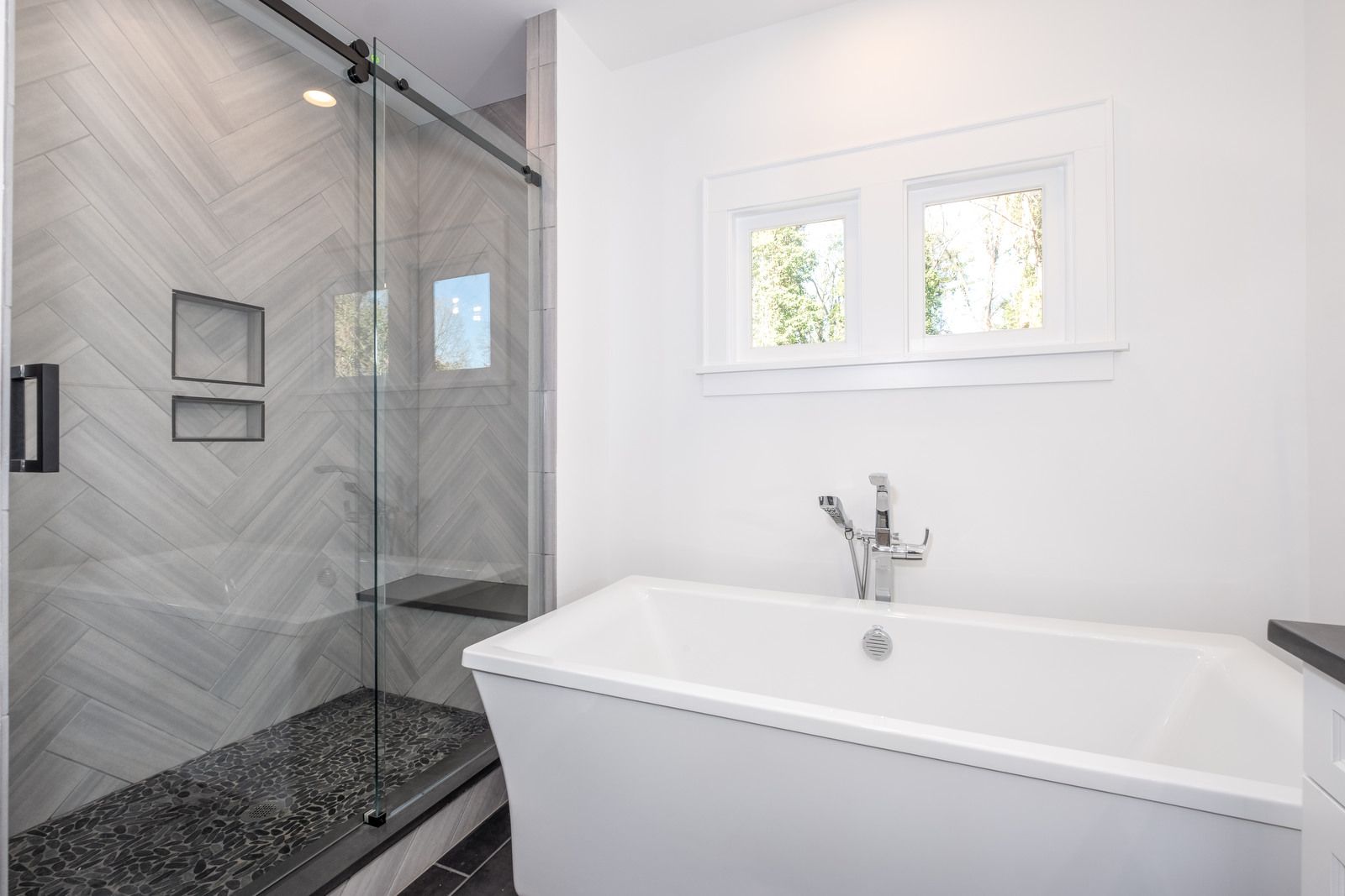Bathroom with a freestanding tub, a glass shower with herringbone tile, and a pair of small windows