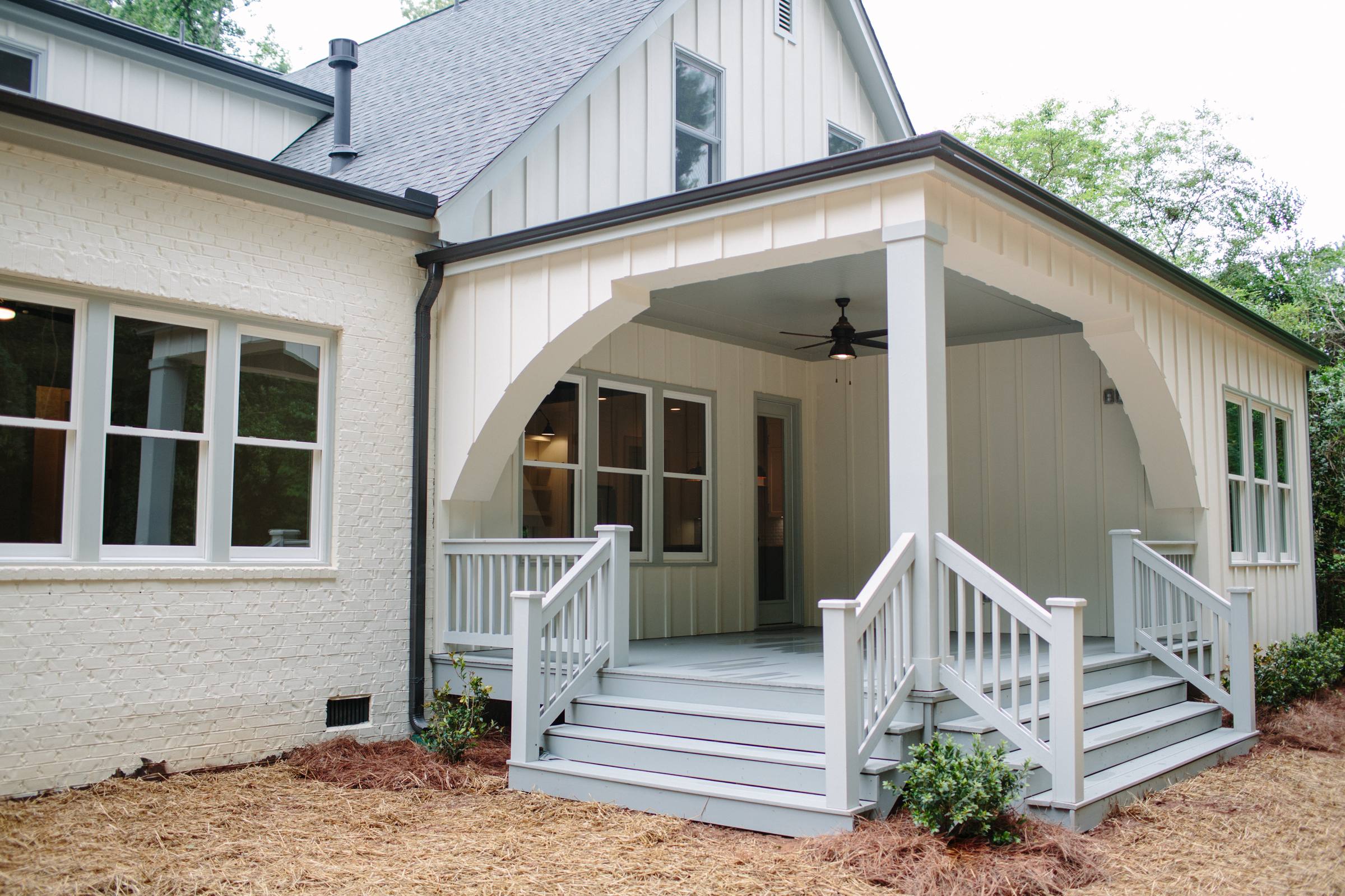 White brick home with a covered back porch, arched trim, and painted wood steps and railings
