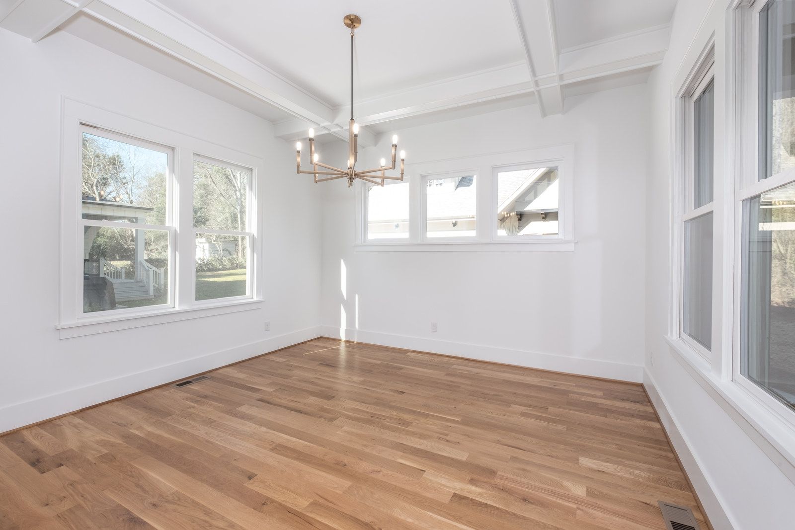 Empty dining room with a beamed ceiling, a brass chandelier, hardwood floors, and windows on three sides