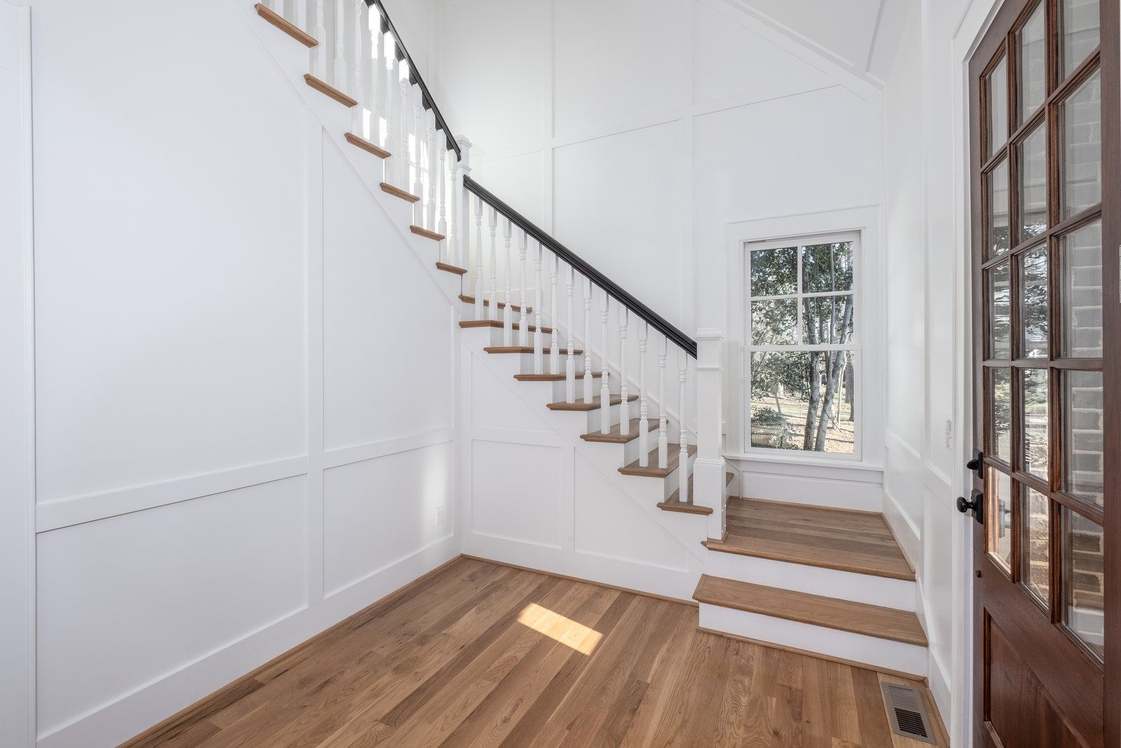 Entry with white paneled walls, a staircase with wood treads, and a wood front door with glass panes