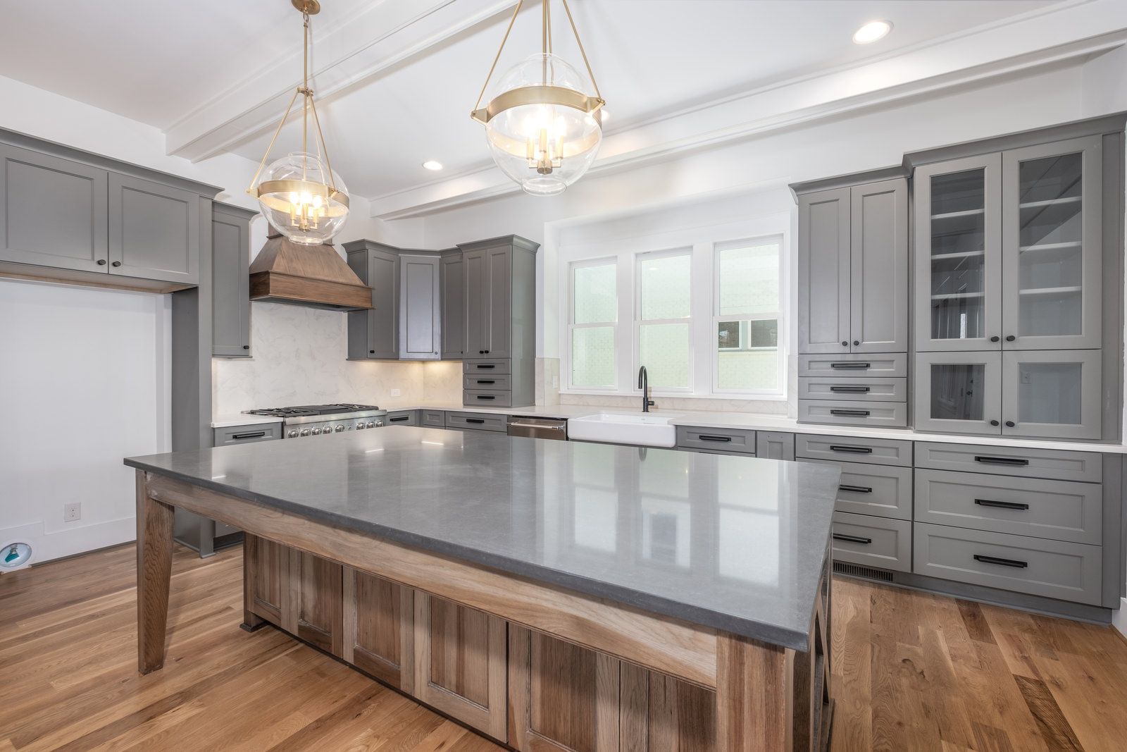 Kitchen with gray cabinets, a wood-base island with a dark top, glass pendants, and a beamed ceiling