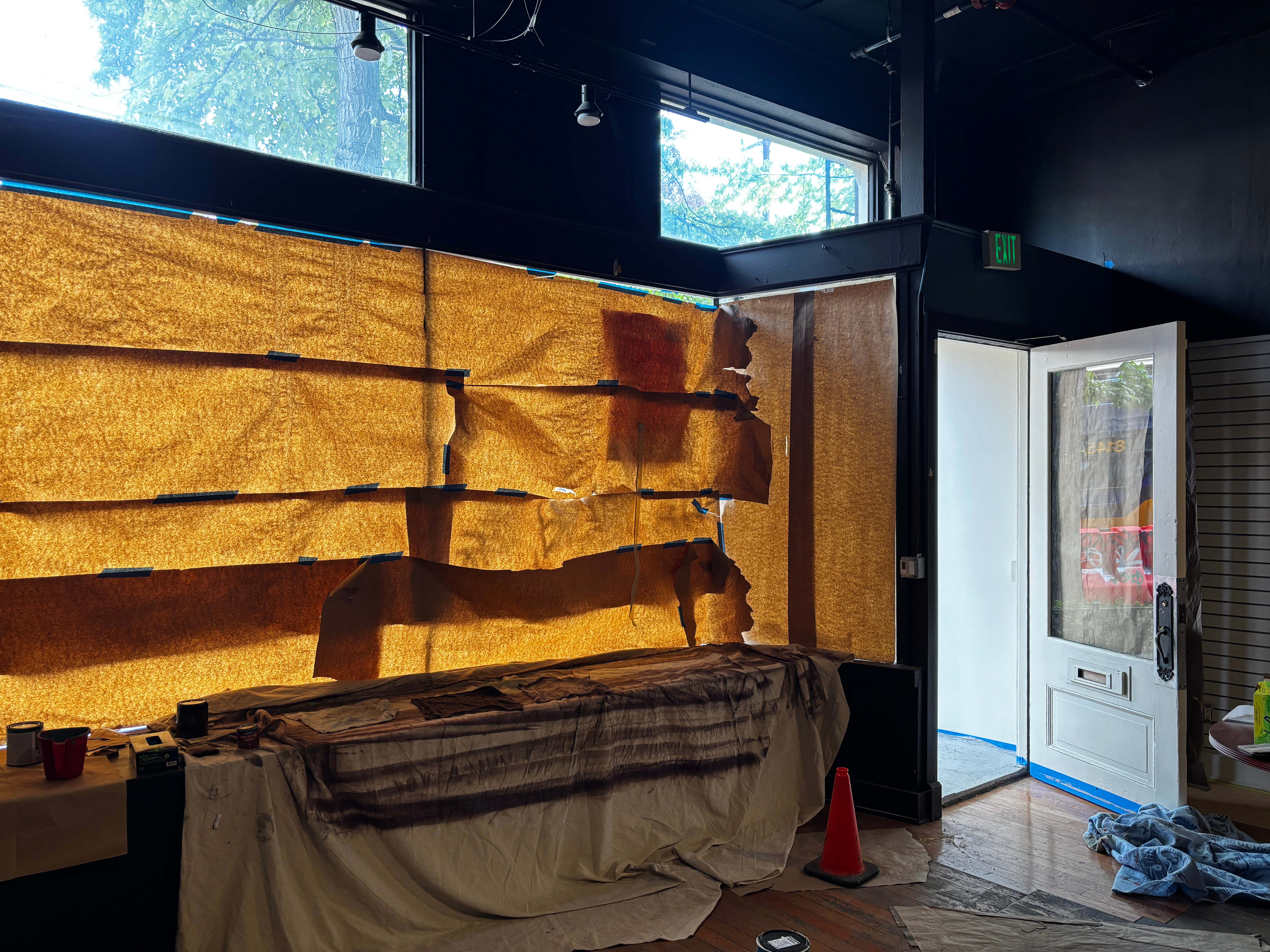Room with windows covered in torn brown paper, open white door, and covered furniture inside.