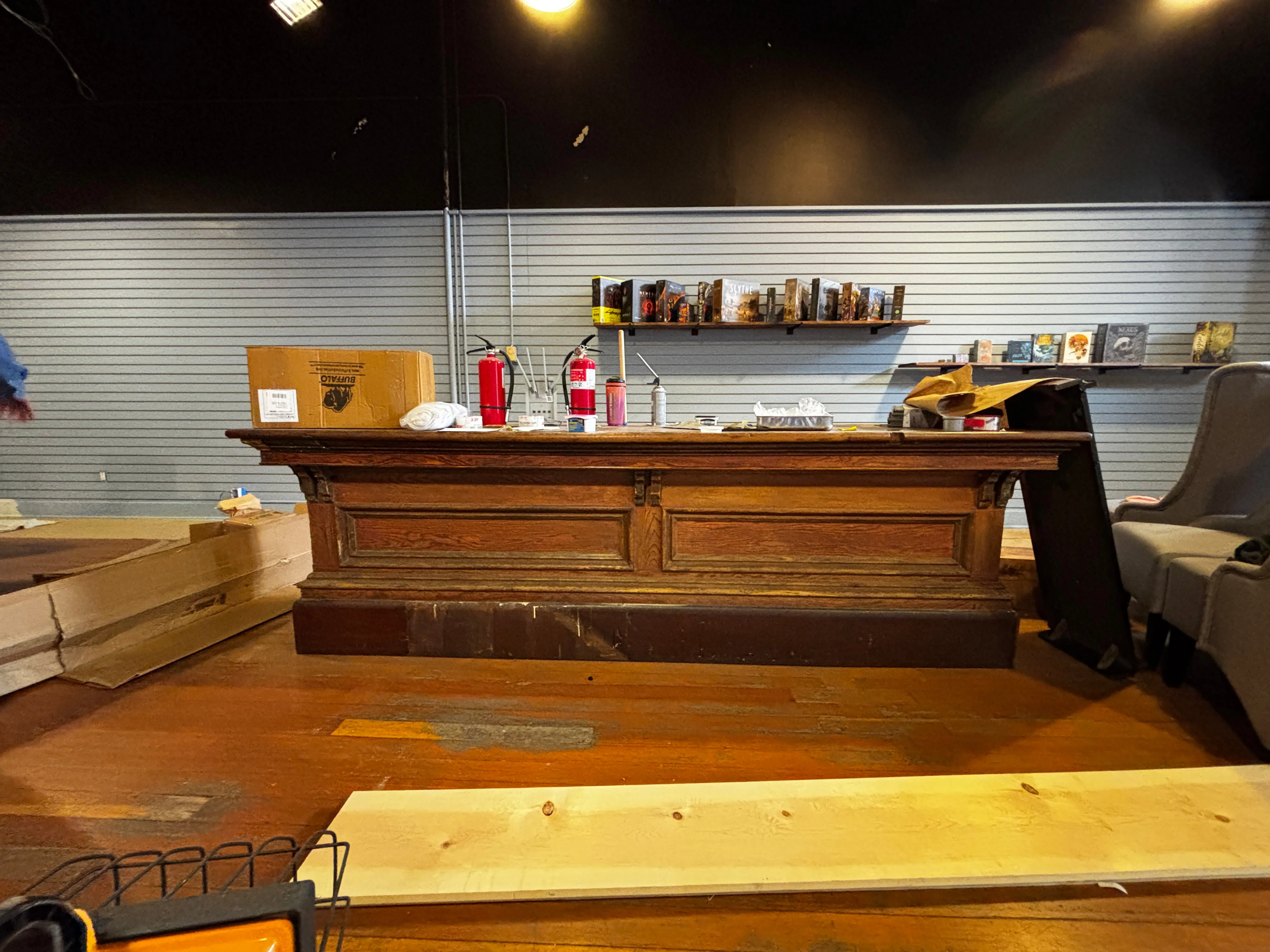 Old wooden counter with two fire extinguishers and various items on top in a room with grey slat wall panels.