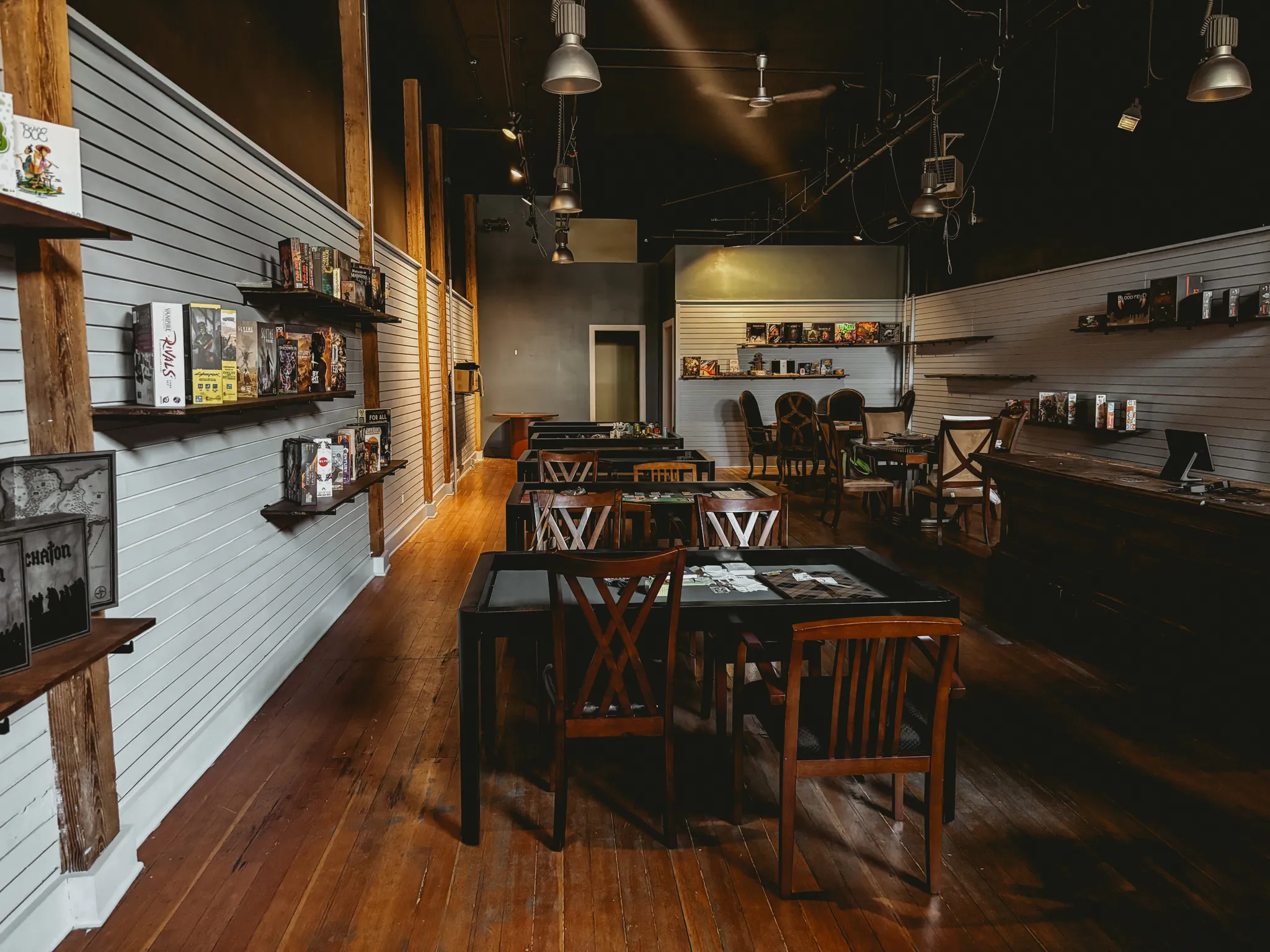 Interior of a board game cafe with wooden floors, tables, chairs, and shelves of games.