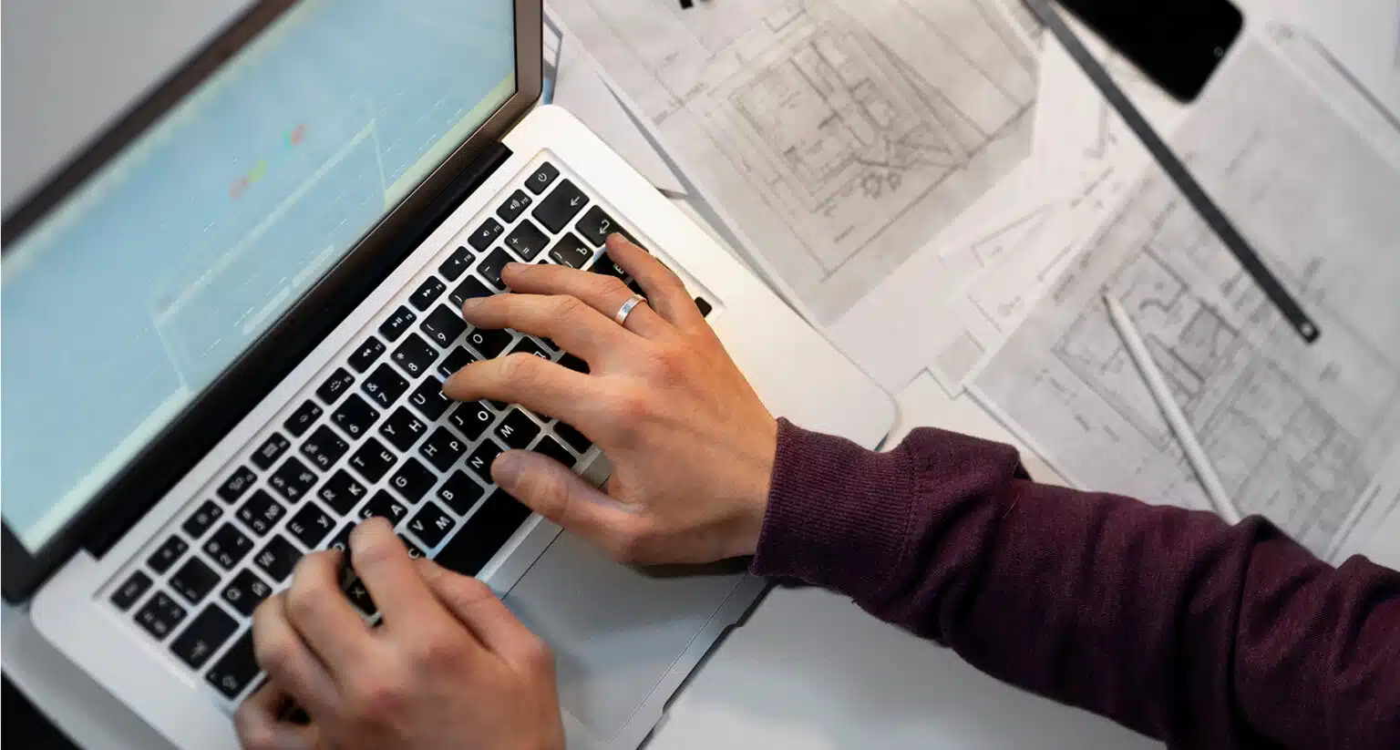 Person typing on laptop while looking at blueprint papers