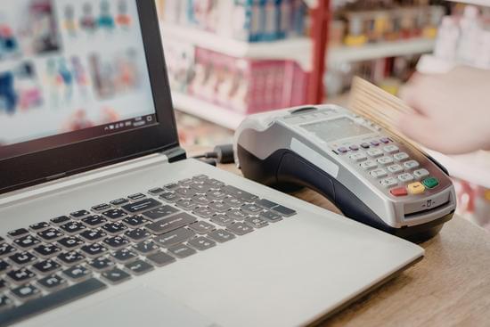 Terminal de pagamento ao lado de um laptop sobre um balcão