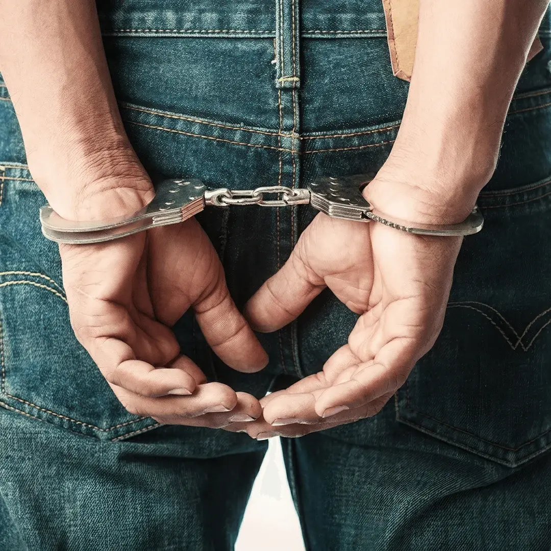 A close-up shot shows a young person's hands cuffed behind their back, jeans visible in the frame.