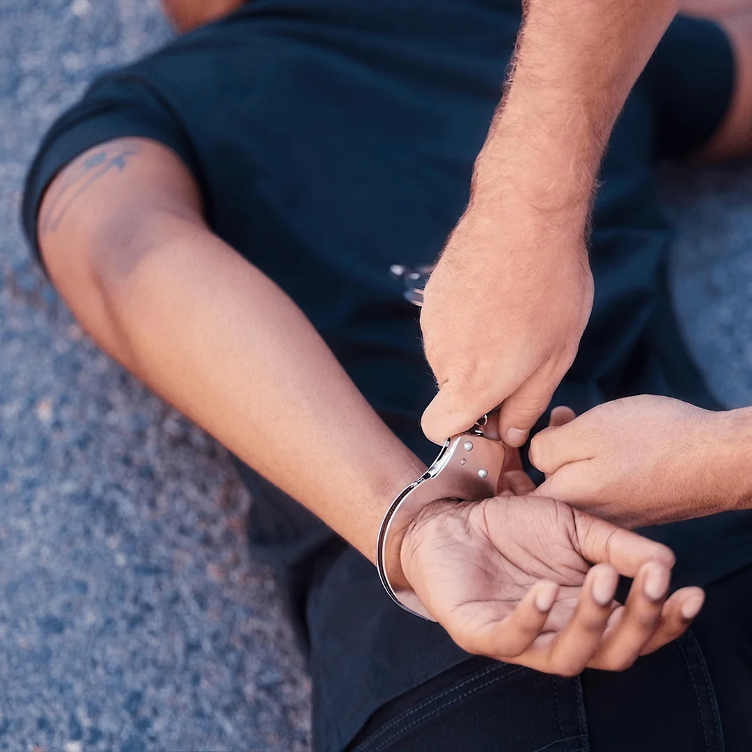 A law enforcement officer places handcuffs on a seated individual's wrist during an arrest.