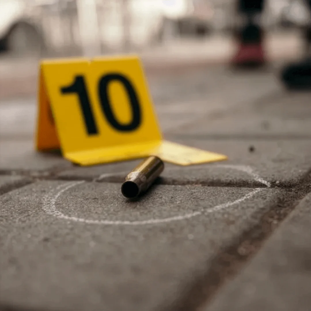 A numbered evidence marker sits beside a spent shell casing at an outdoor crime scene.