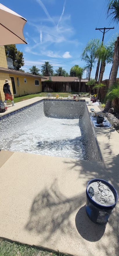 Empty rectangular pool being replastered in a backyard with palm trees and a person nearby.