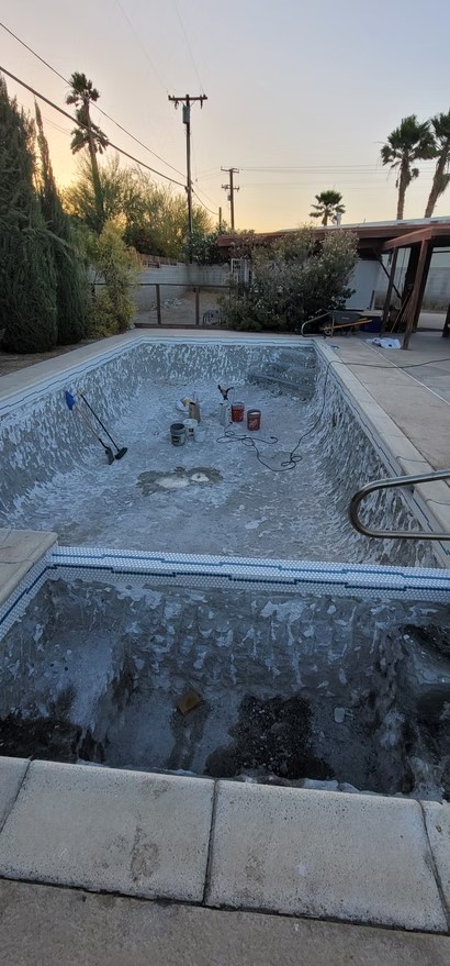 Empty residential pool undergoing replastering with tools and buckets inside during sunset.