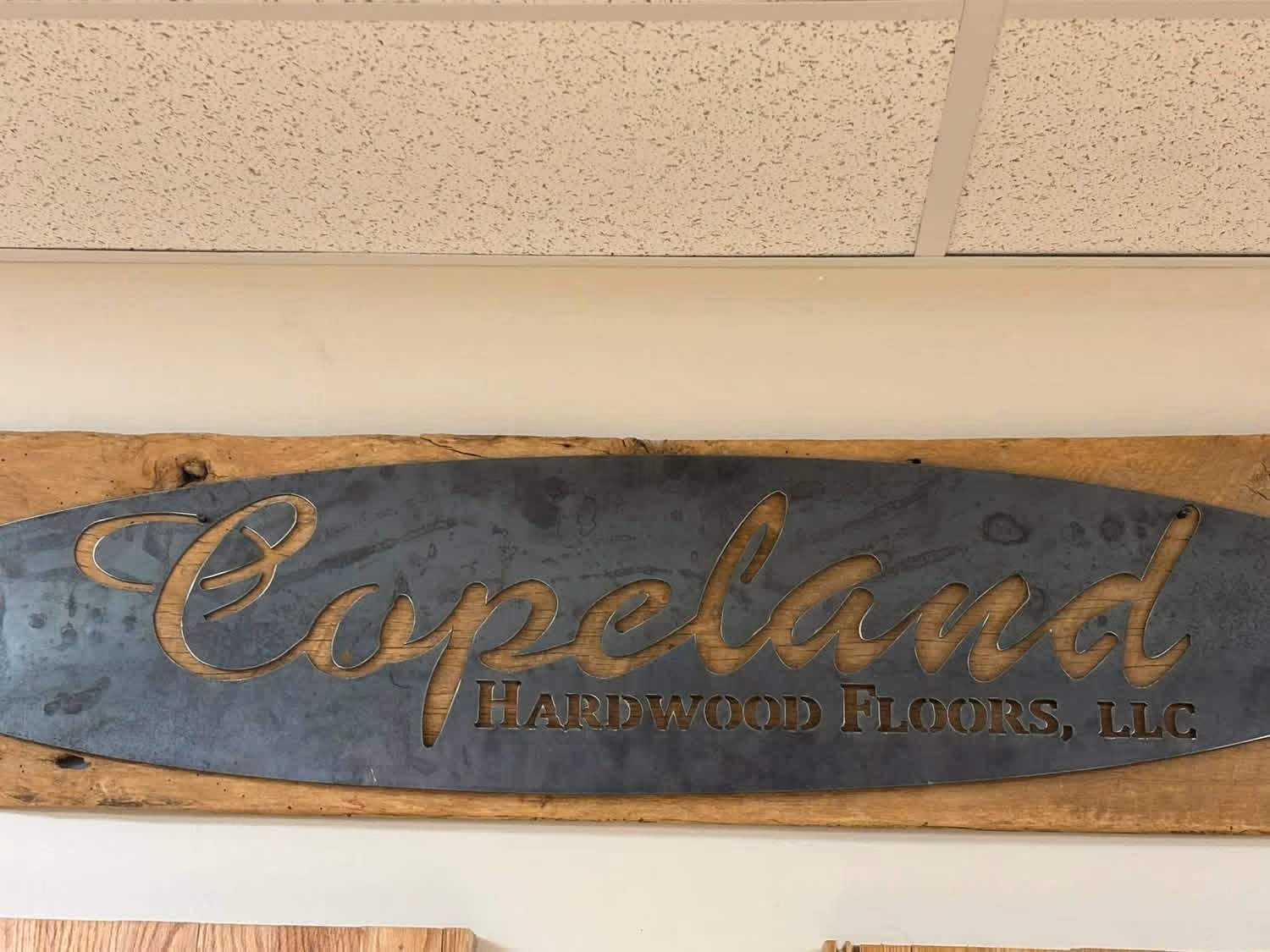 Metal sign mounted on wood reading Copeland Hardwood Floors, LLC on an office wall.