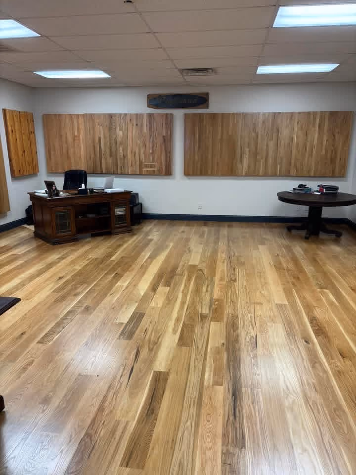 Office room with polished wooden floor, two wooden desks, and wood panel art on white walls.