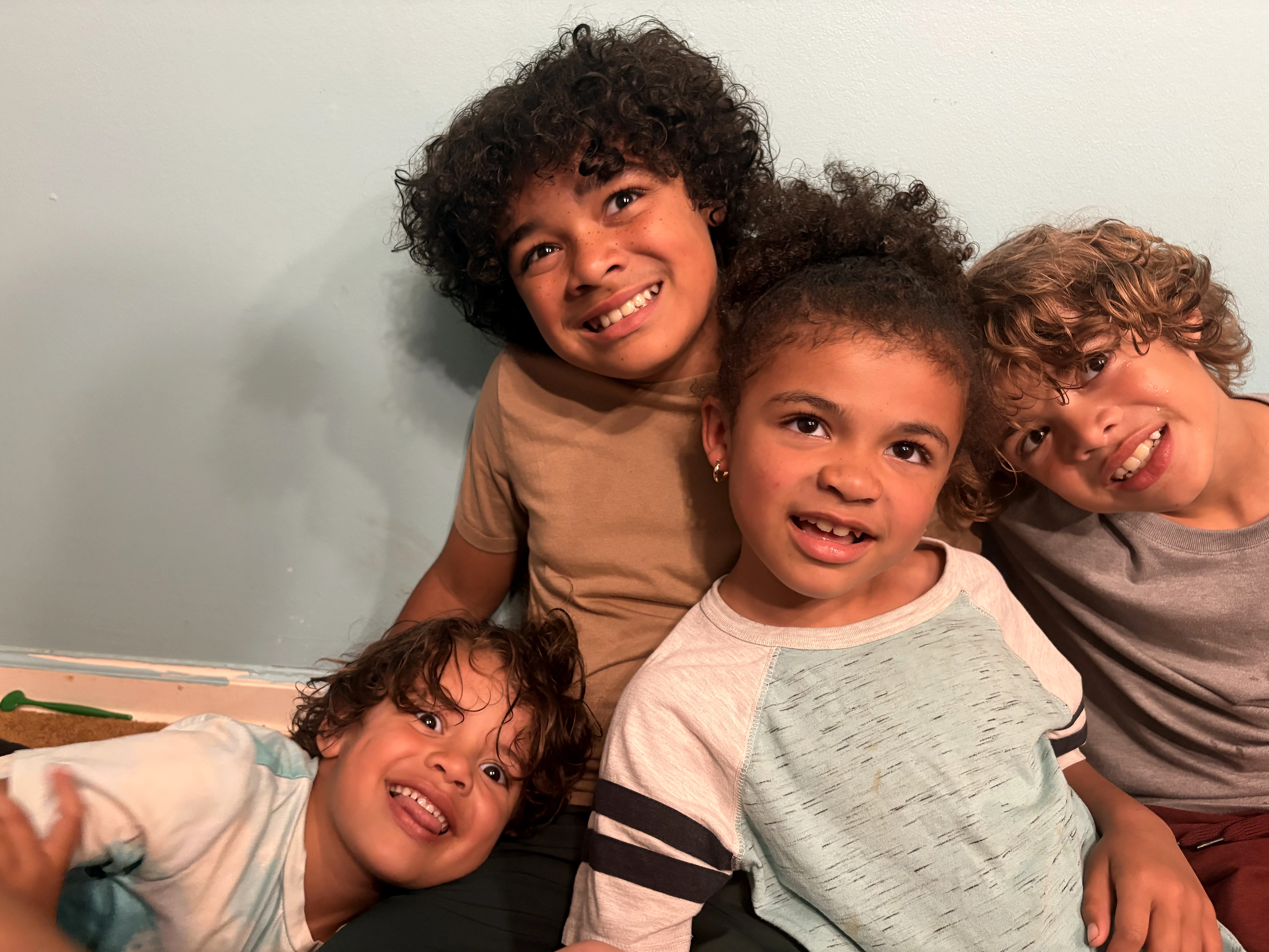 Four smiling curly-haired kiddos posing together against a white wall