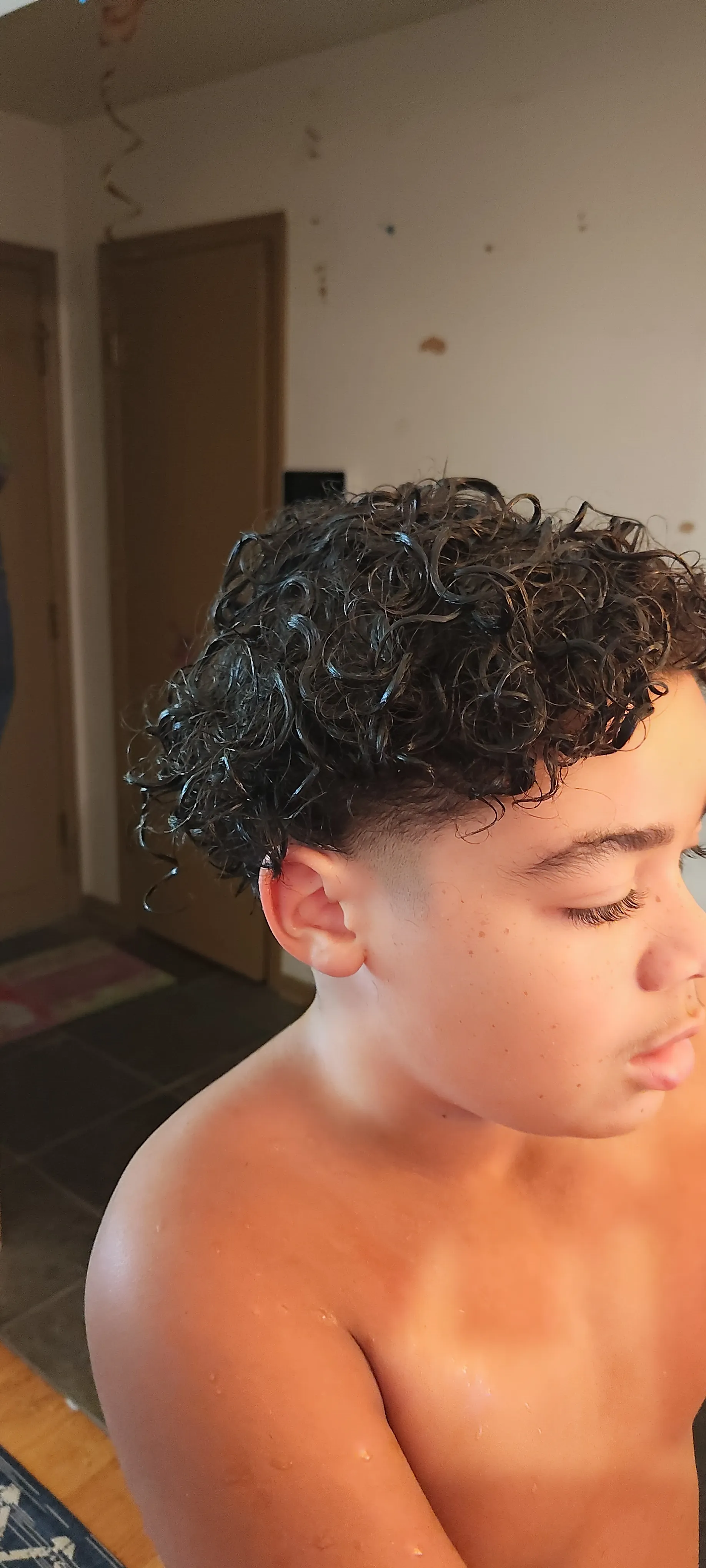 Close-up of wet, defined dark curls on top of a fade haircut