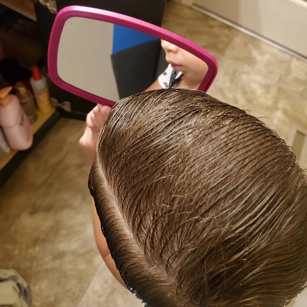 Overhead view of freshly combed wet curls as a kiddo checks them in a pink hand mirror