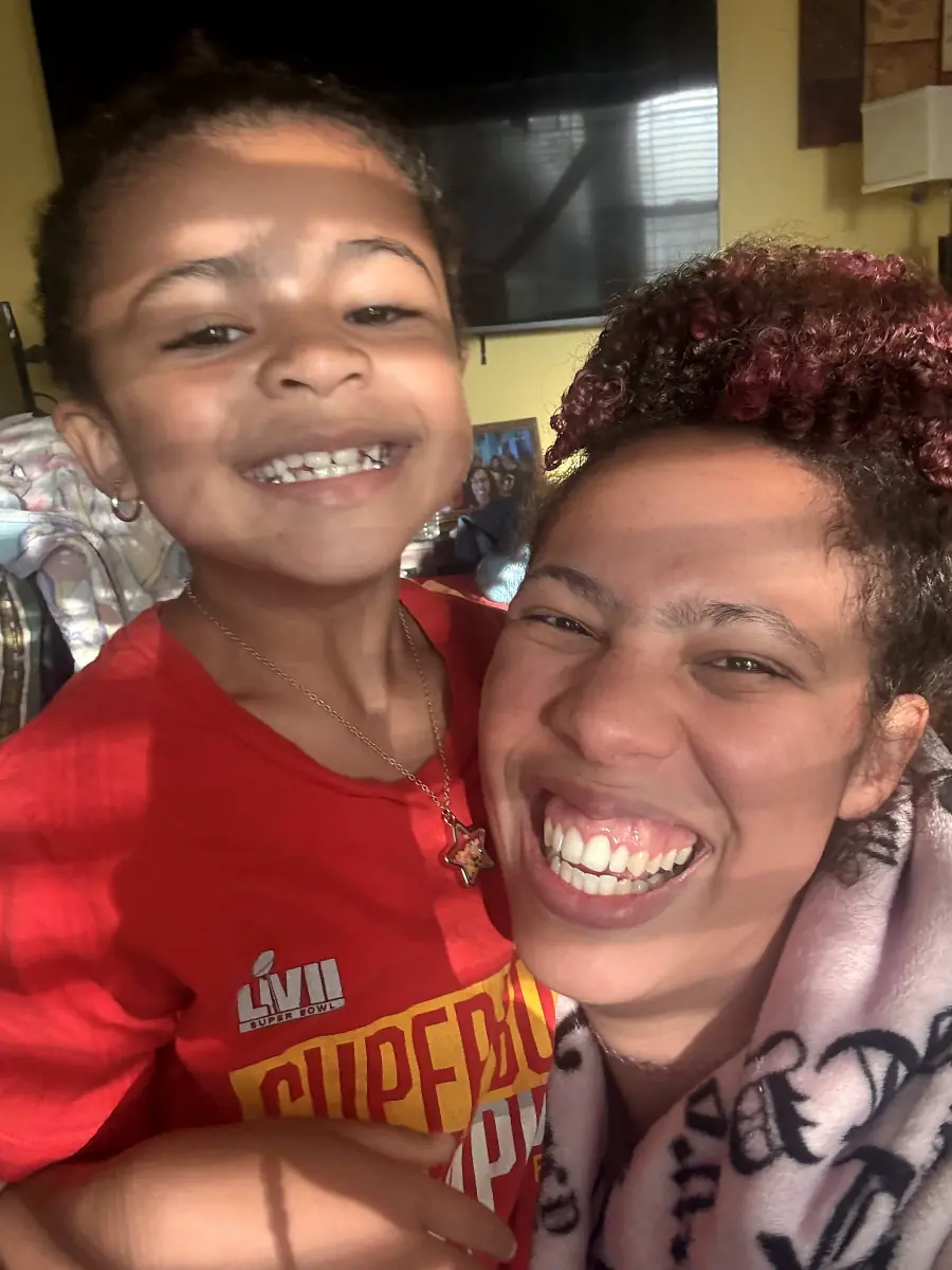 A curly-haired parent and child smiling together in a selfie