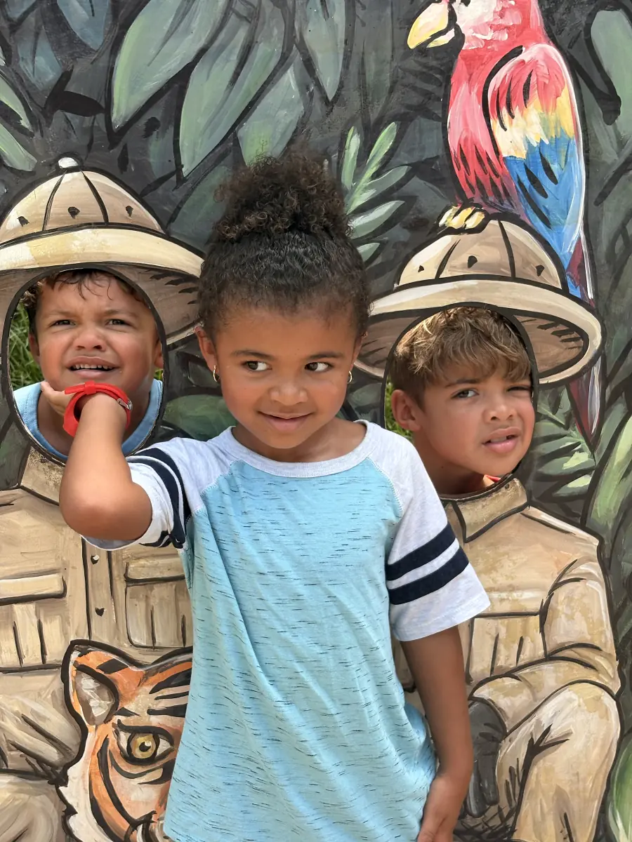 Three curly-haired kiddos posing in front of a jungle mural