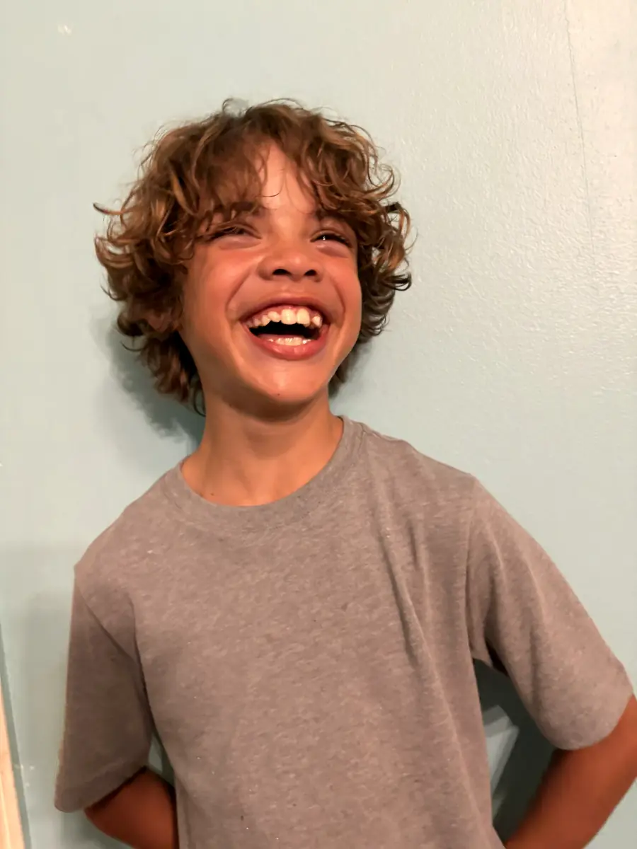 Curly-haired boy laughing against a light blue wall