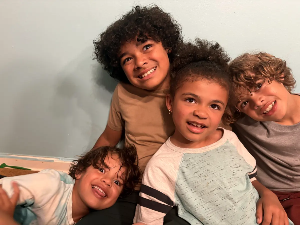 Four smiling curly-haired kiddos posing together against a white wall
