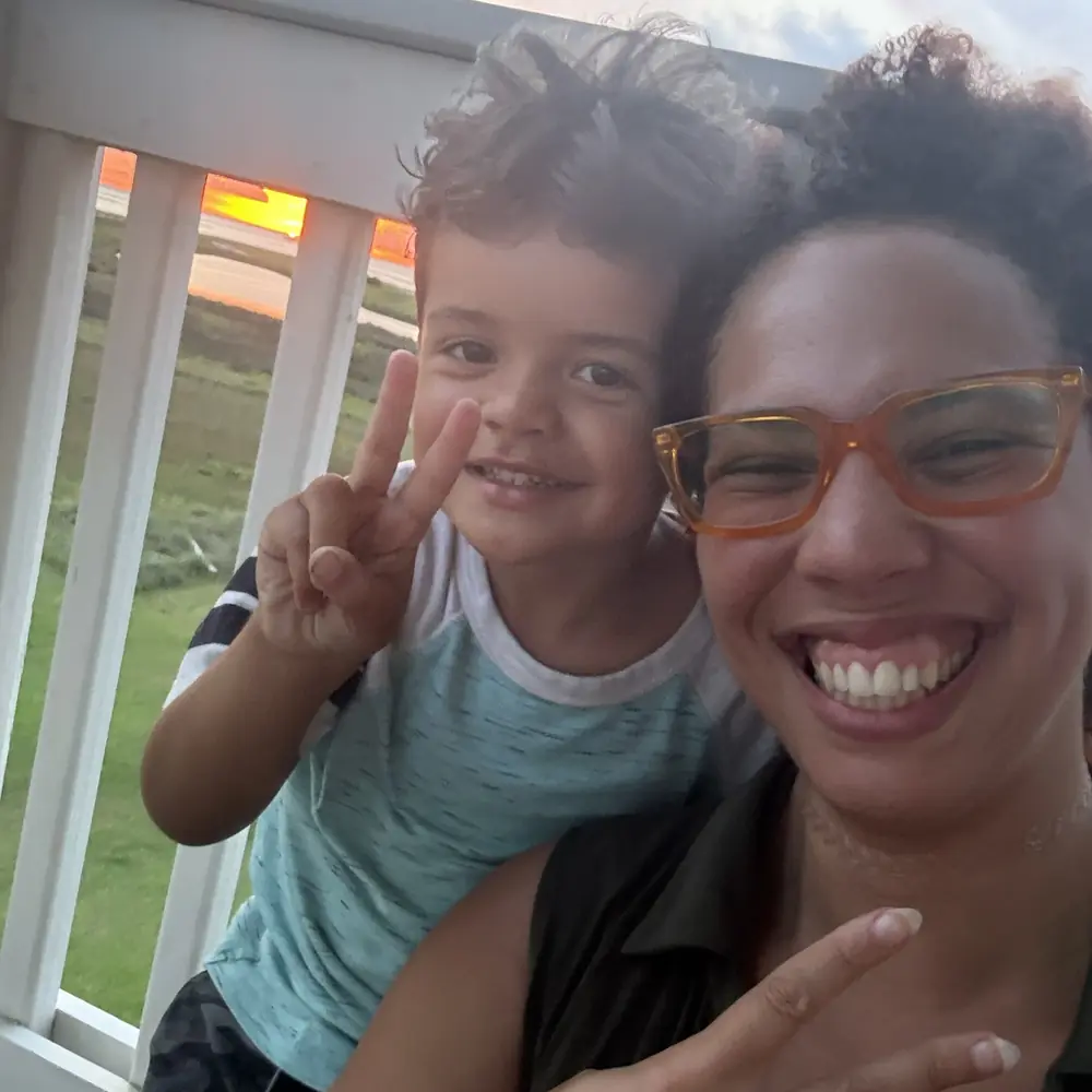 Just So Curly founder Cassandra smiling in a selfie with a curly-haired boy flashing a peace sign