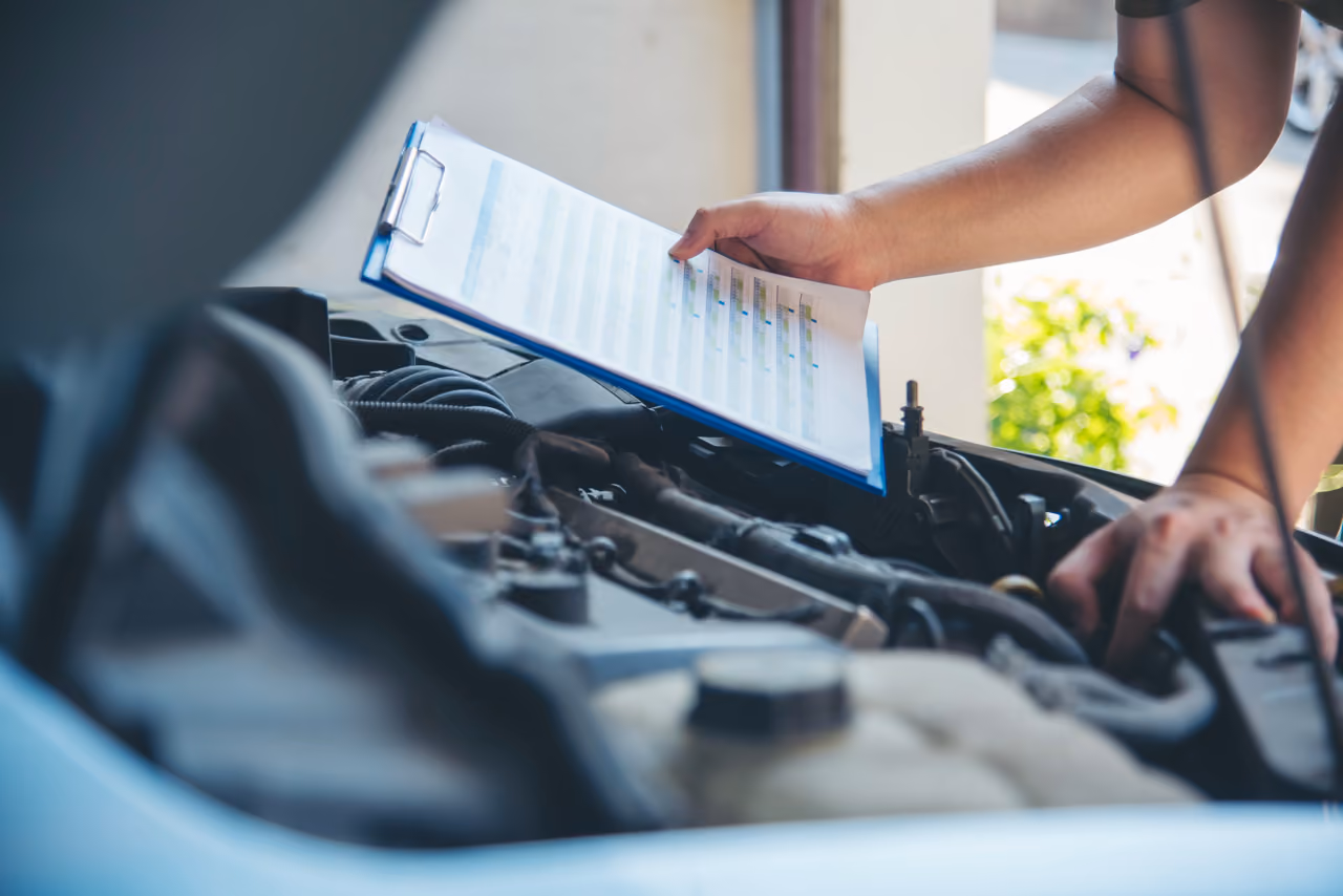 Mechanic working through a checklist under the bonnet during a pre-purchase car inspection