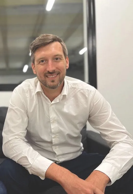 Homme souriant portant une chemise blanche assis sur un canapé dans un bureau moderne.