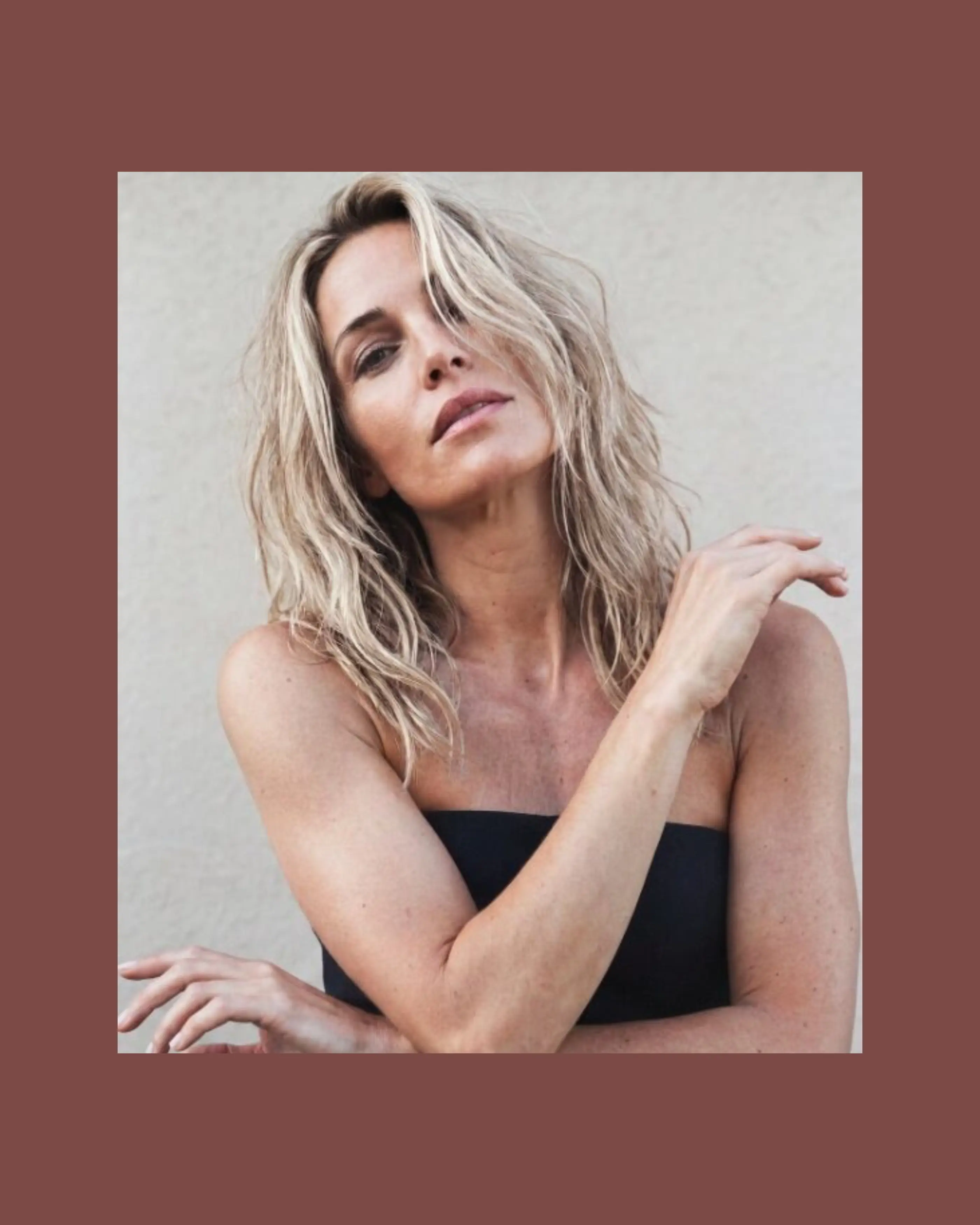 A cute blonde woman with blue eyes looking at the camera with crossed arms.