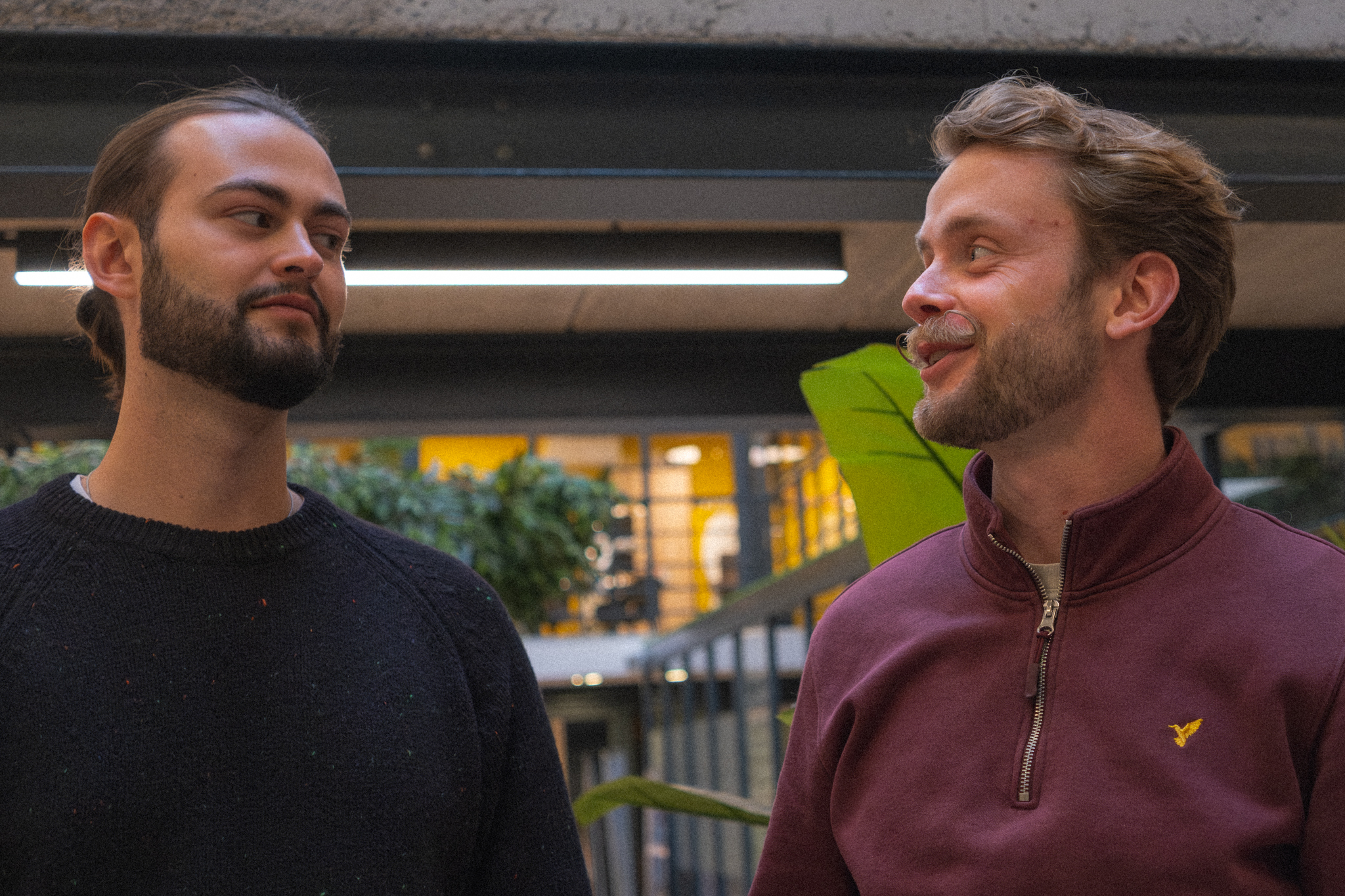Deux hommes se regardant et discutant dans un espace de bureau moderne avec des plantes en arrière-plan.