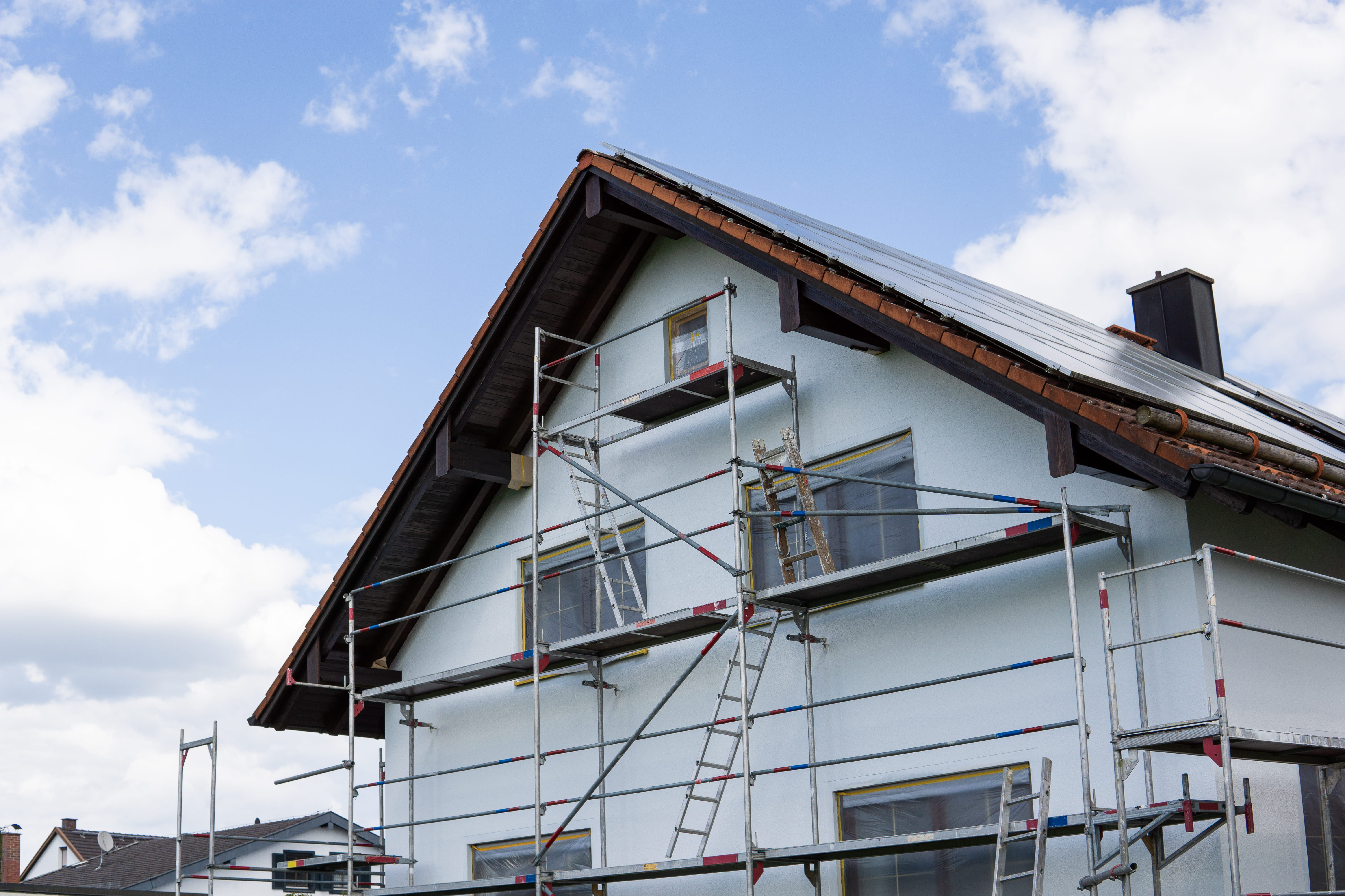 Haus mit weißer Fassade im Bau, mit Gerüst, Leitern und Solarmodulen auf dem Dach.