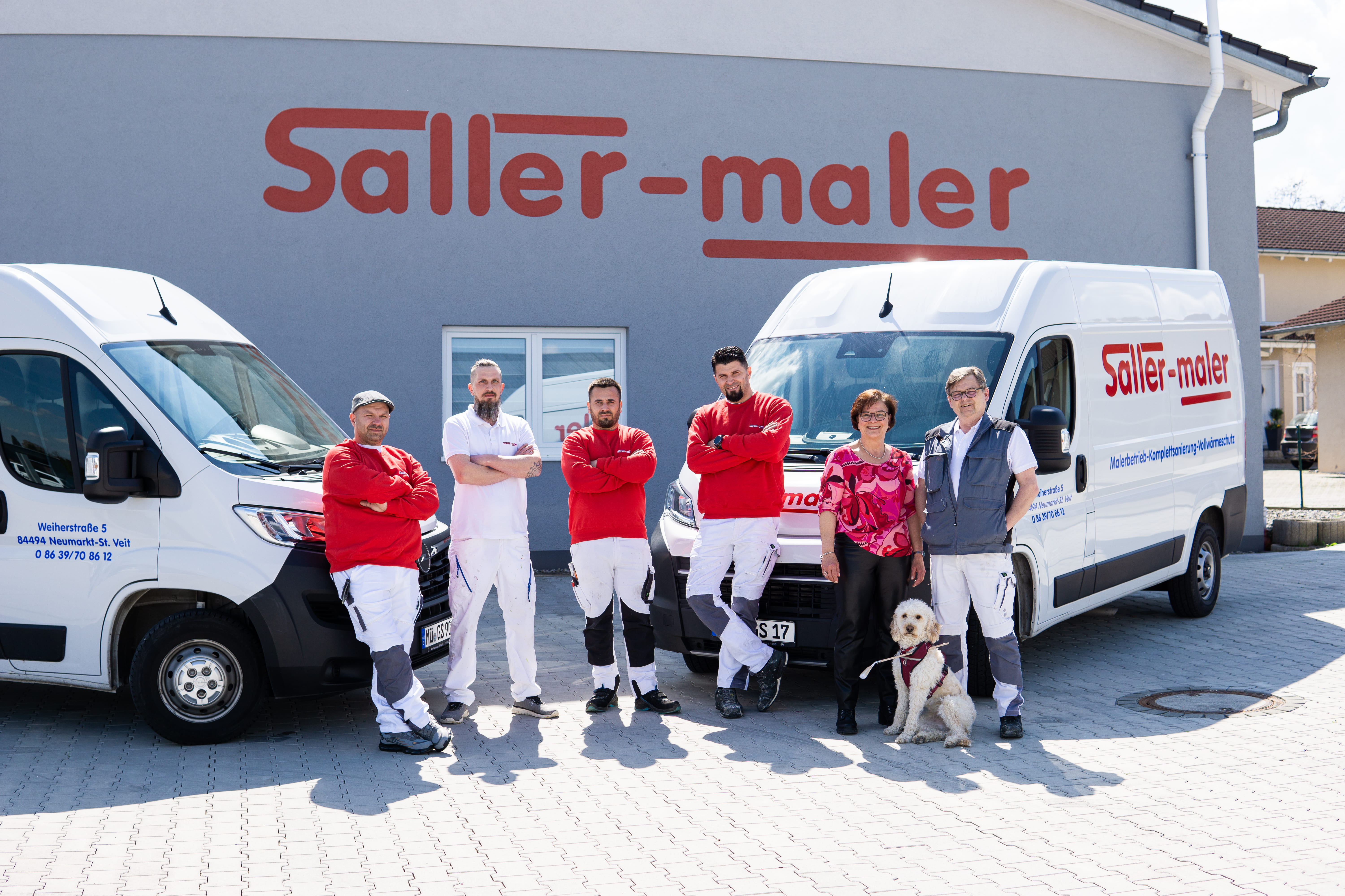 Sechs Personen und ein Hund stehen vor zwei weißen Transportern mit Saller-Maler-Logo.