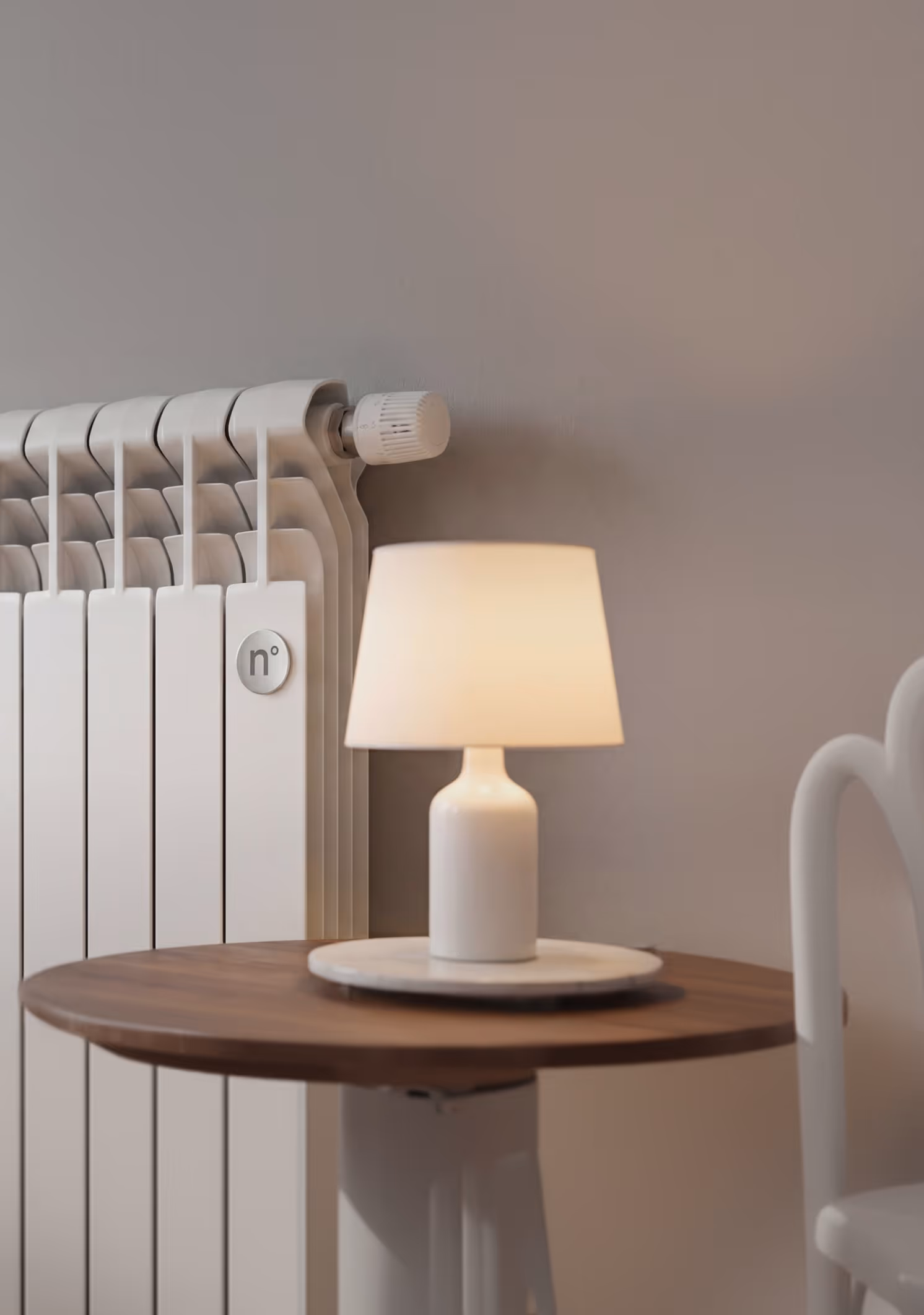 White table lamp on wooden table near white radiator and chair against gray wall.