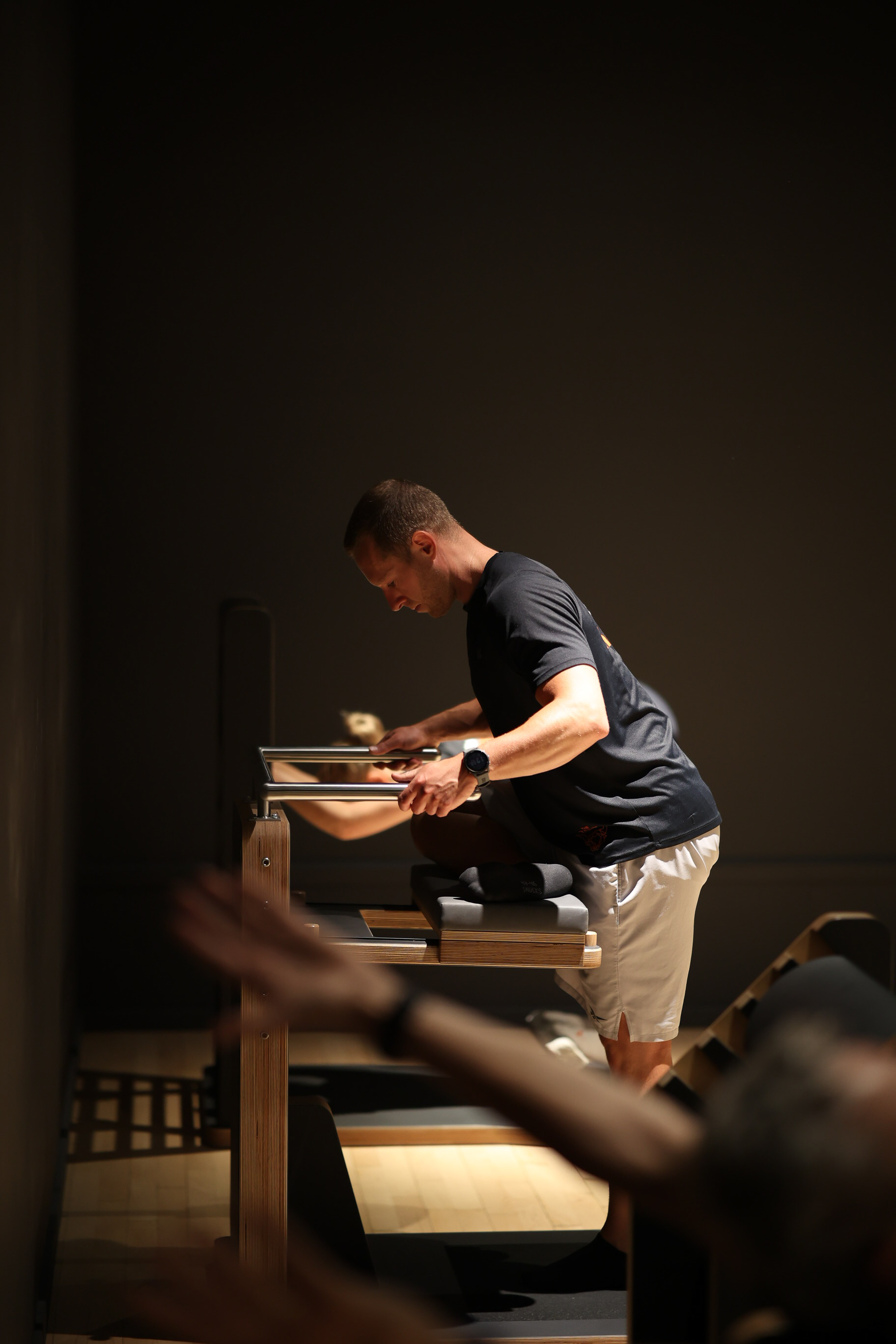 Trainer am Pilates-Reformer während einer Trainingsstunde im abgedunkelten Studio