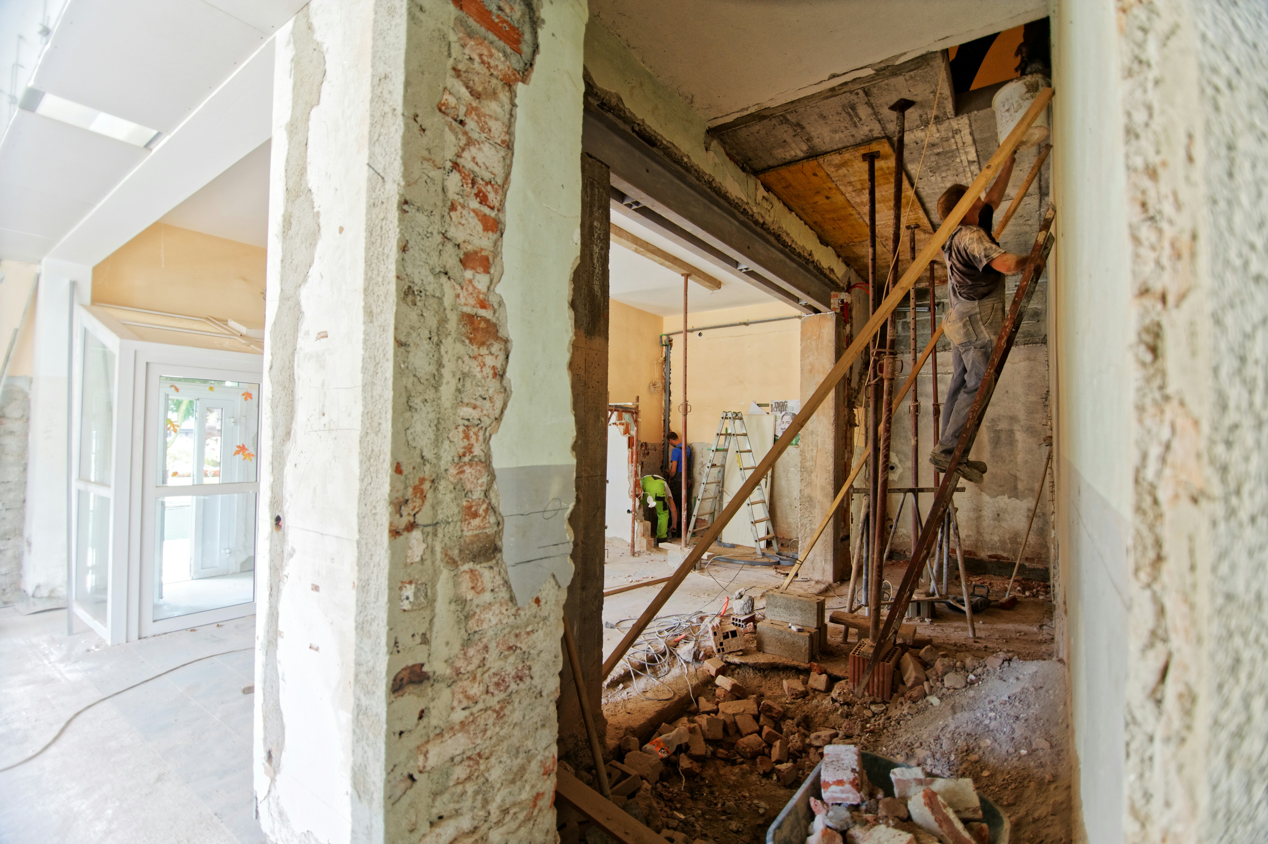 A man standing on a ladder painting a wall in a house that is being renovated.